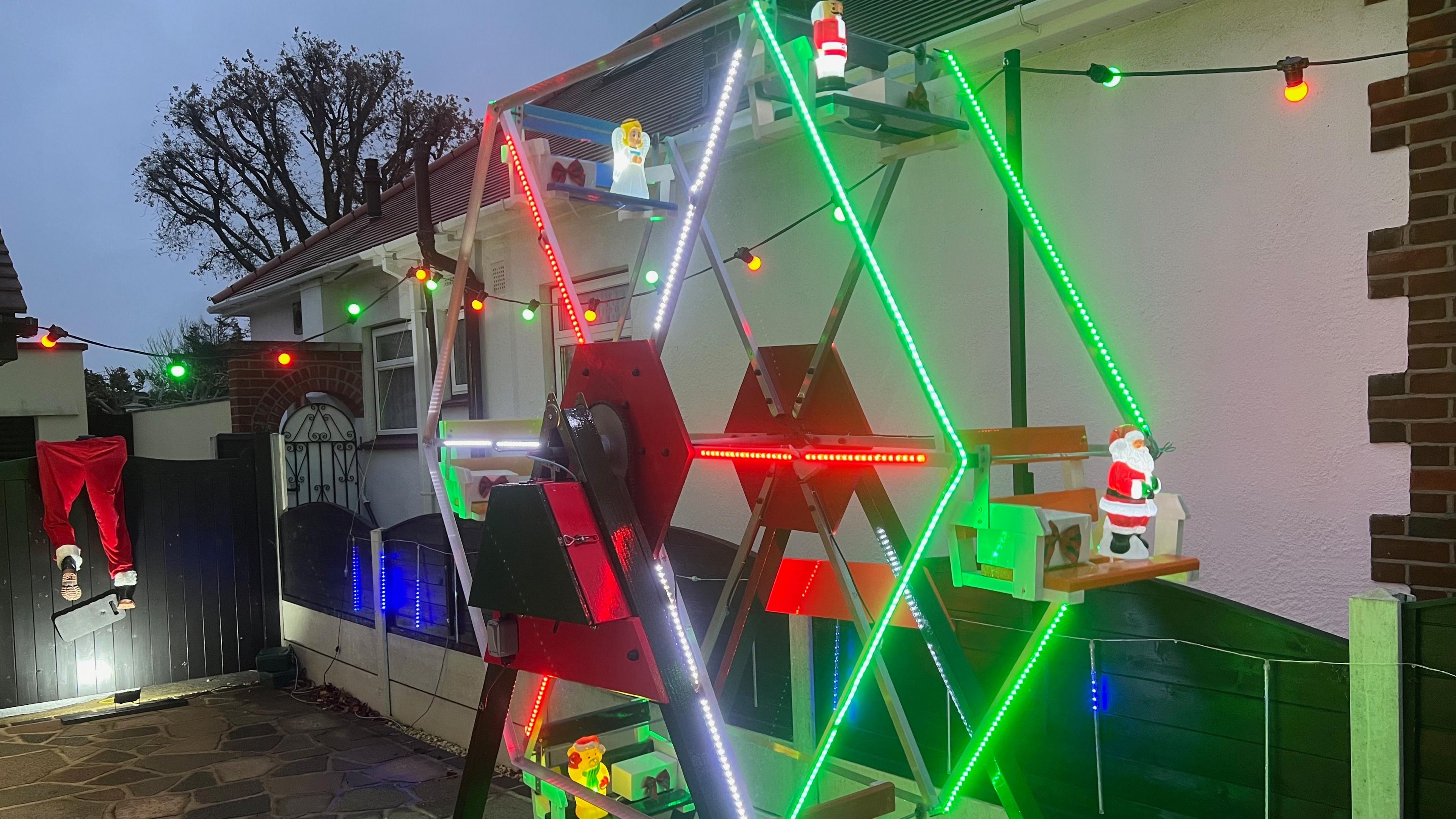 A mechanical Ferris wheel with green, red, and white lights.