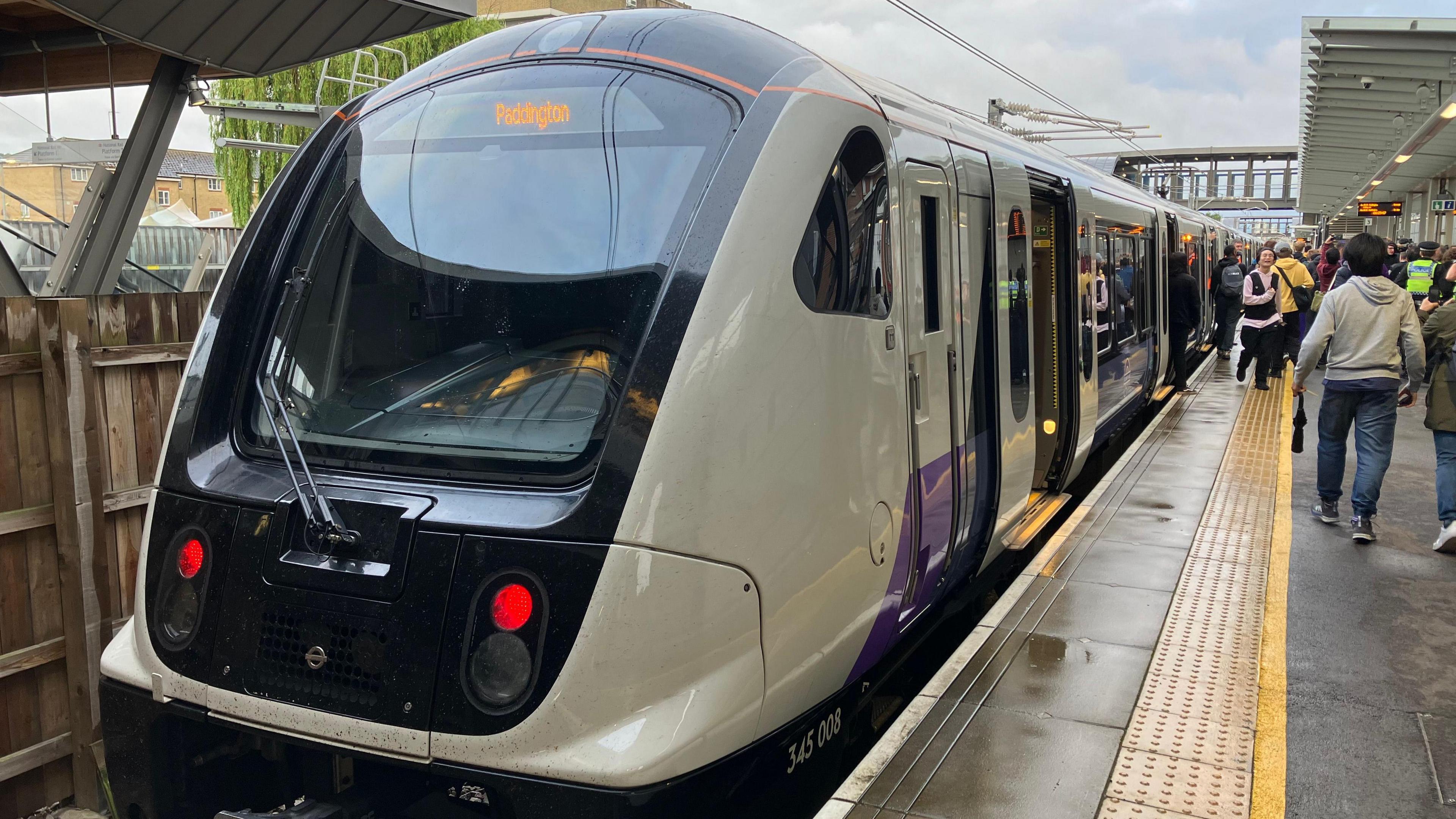 Elizabeth line train with the destination Paddington at a station with people on the move on the platform.