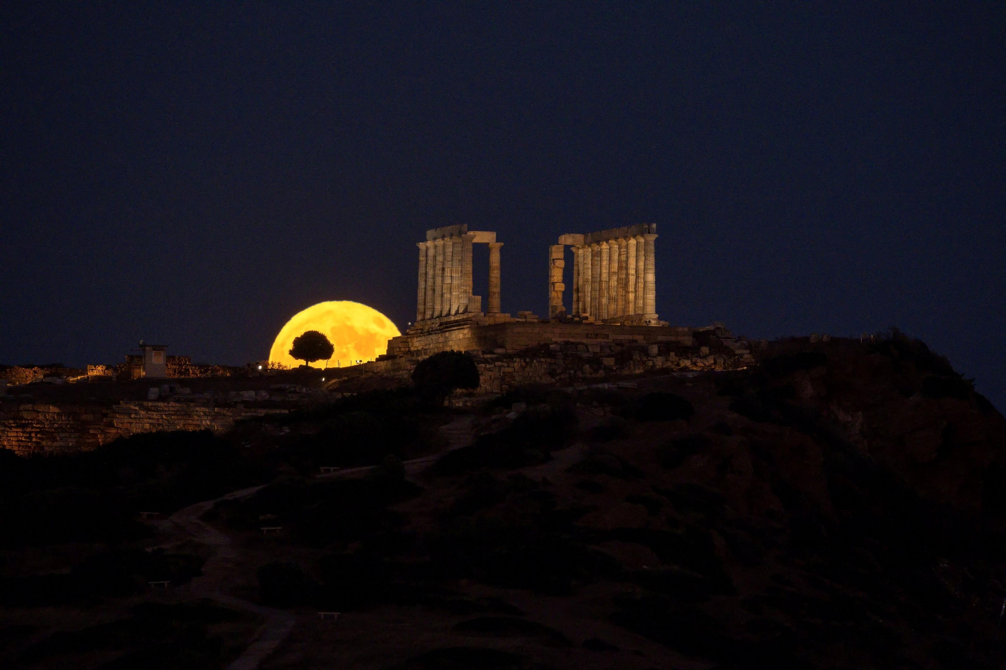 The full Buck Moon rises behind the ancient Temple of Poseidon at Cape Sounion, south of in Athens, Greece