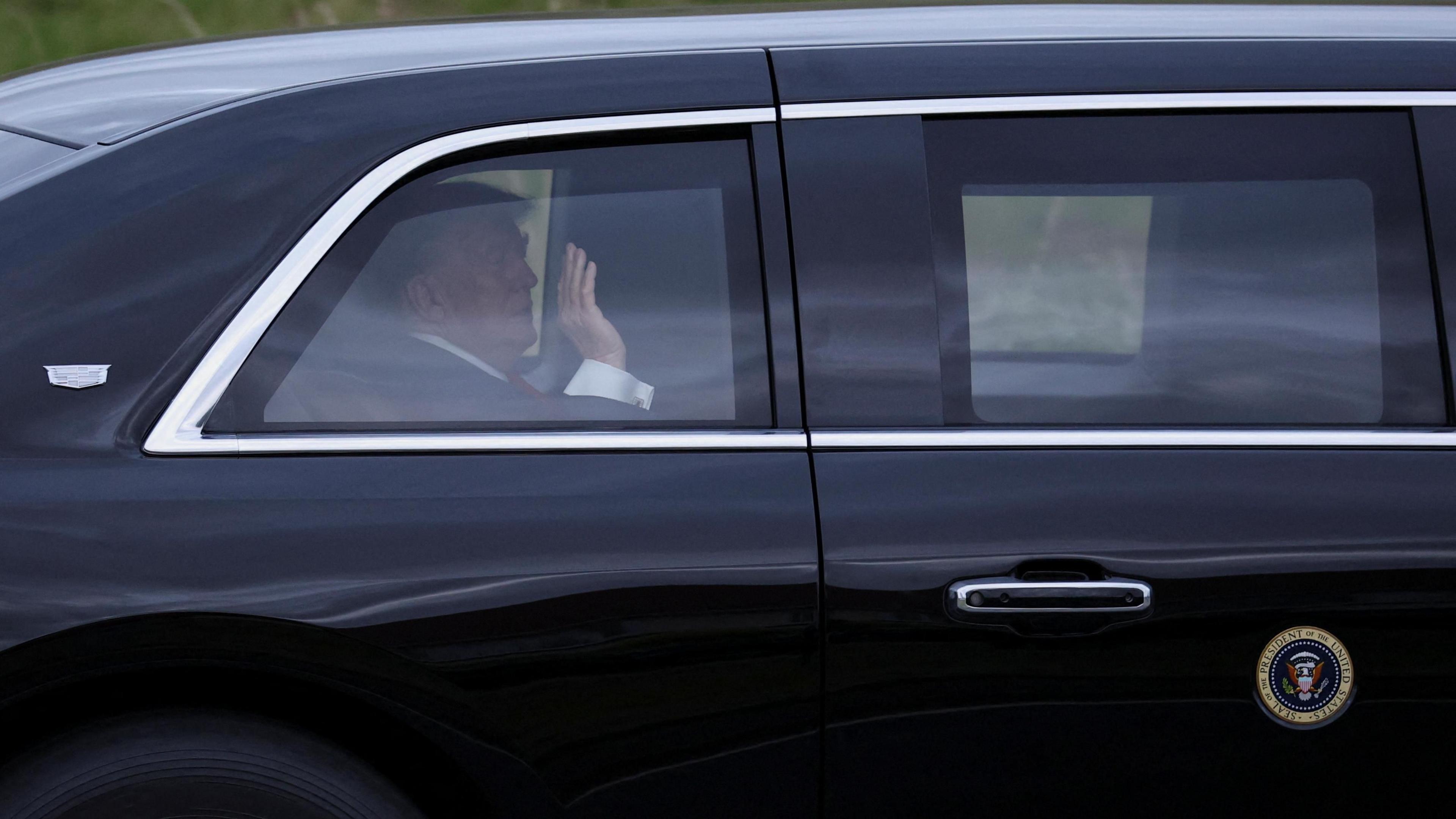 President Donald Trump waves from inside a black vehicle on his way to Turnberry
