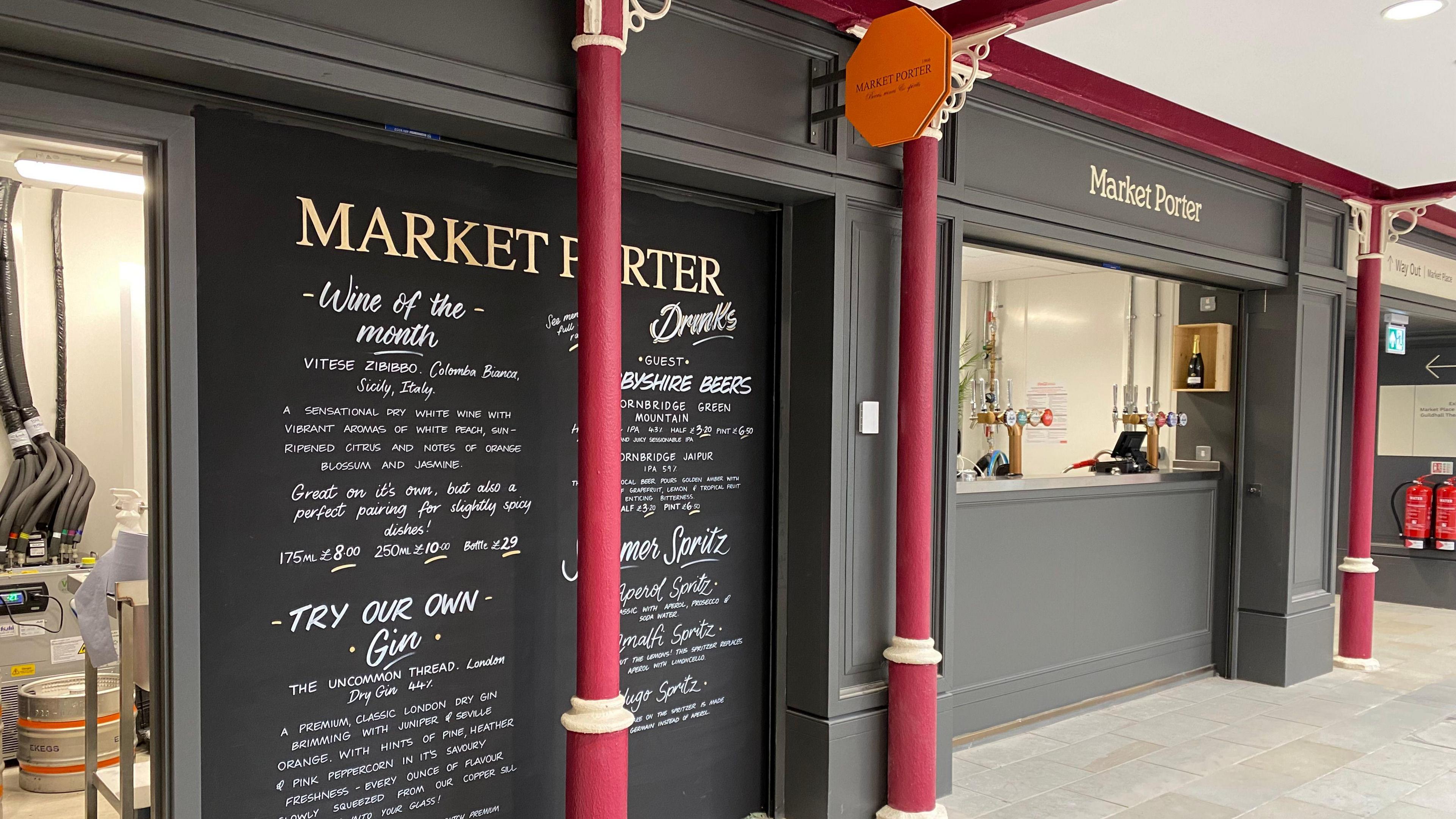 A view of a bar inside Derby Market Hall. There are red posts in front of it with the name "Market Porter" seen above