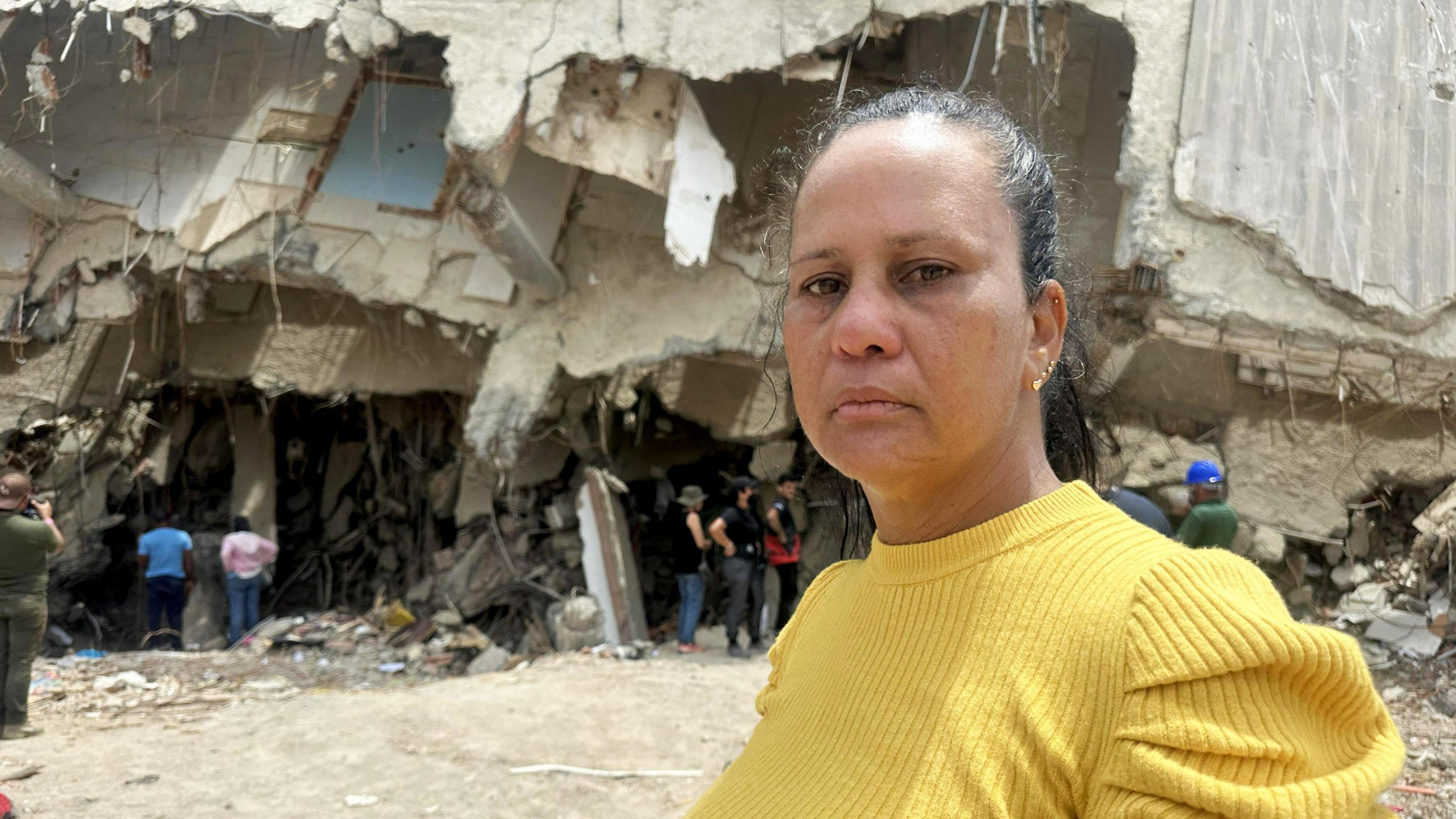 Laura Barrios stands in front of a destroyed apartment block
