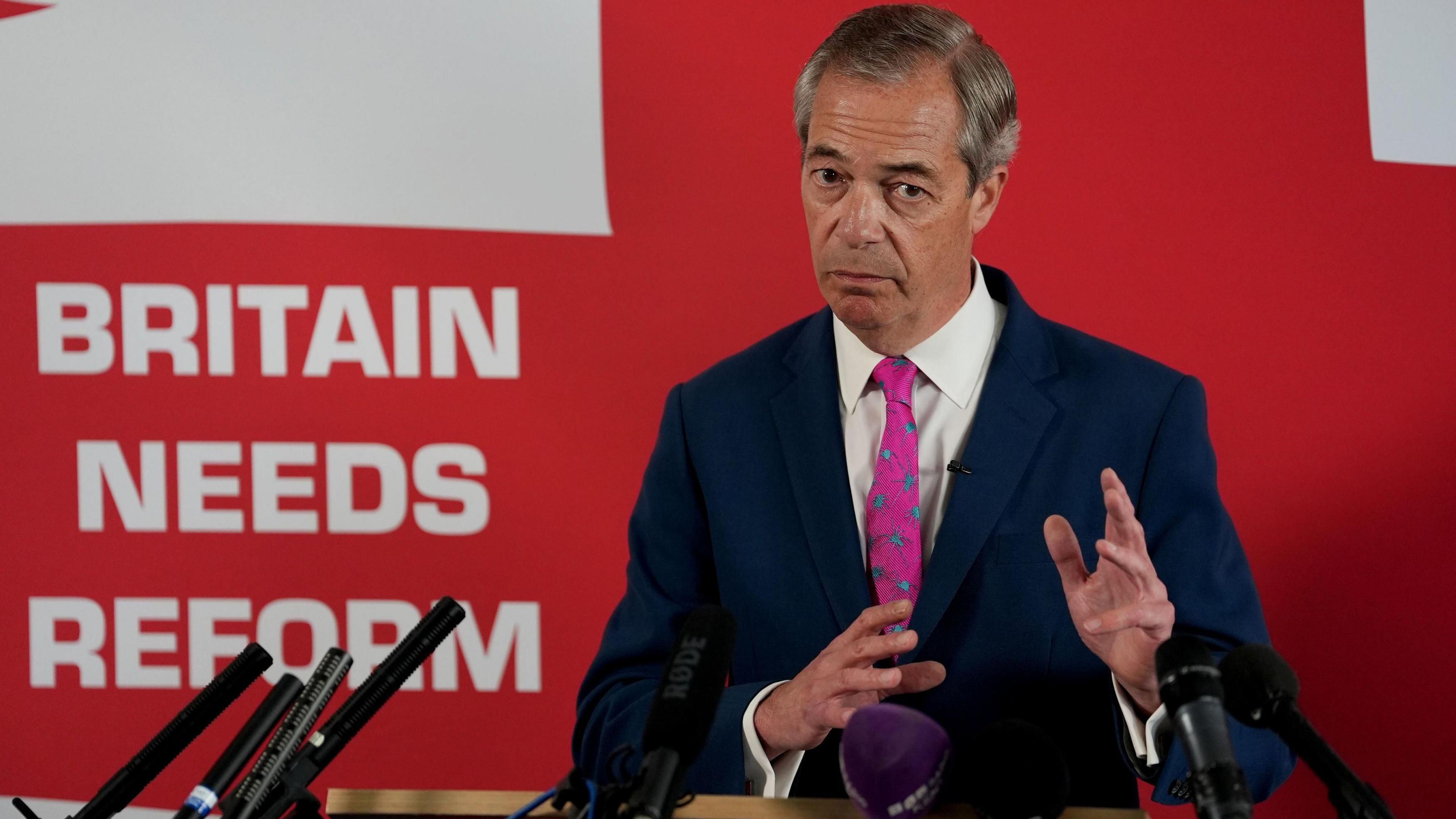 Nigel Farage giving a speech standing in front of a St George's flag which reads 'Britain needs reform'