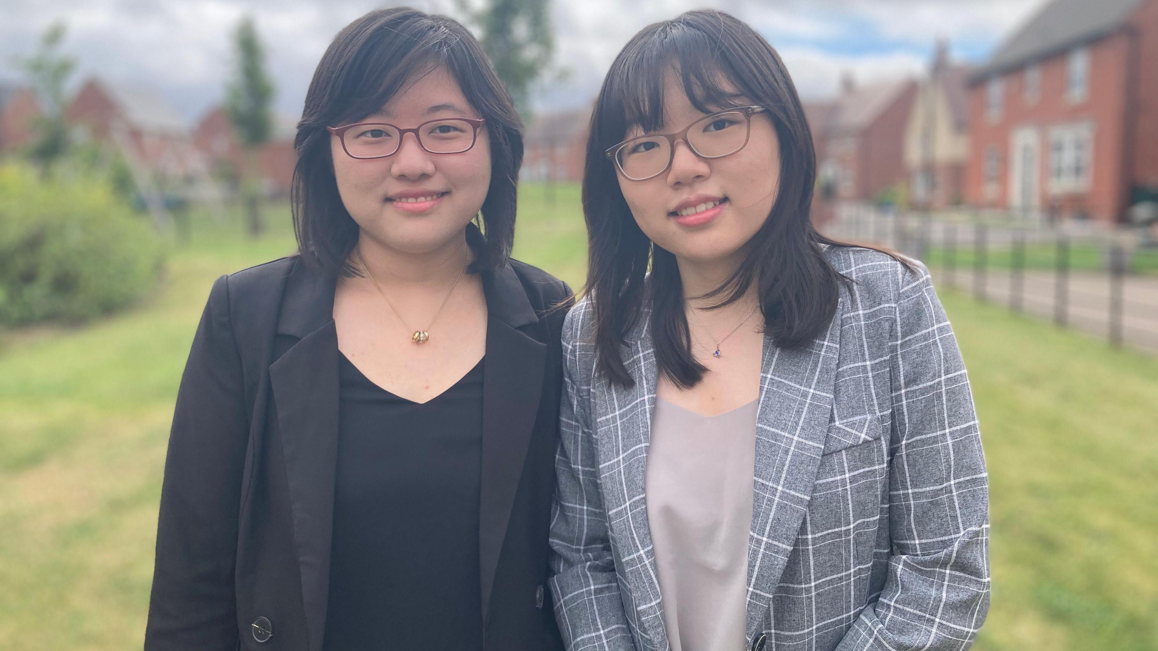 Clara, wearing a black top and jacket, alongside her sister Juliana, wearing a grey checked jacket and grey top.