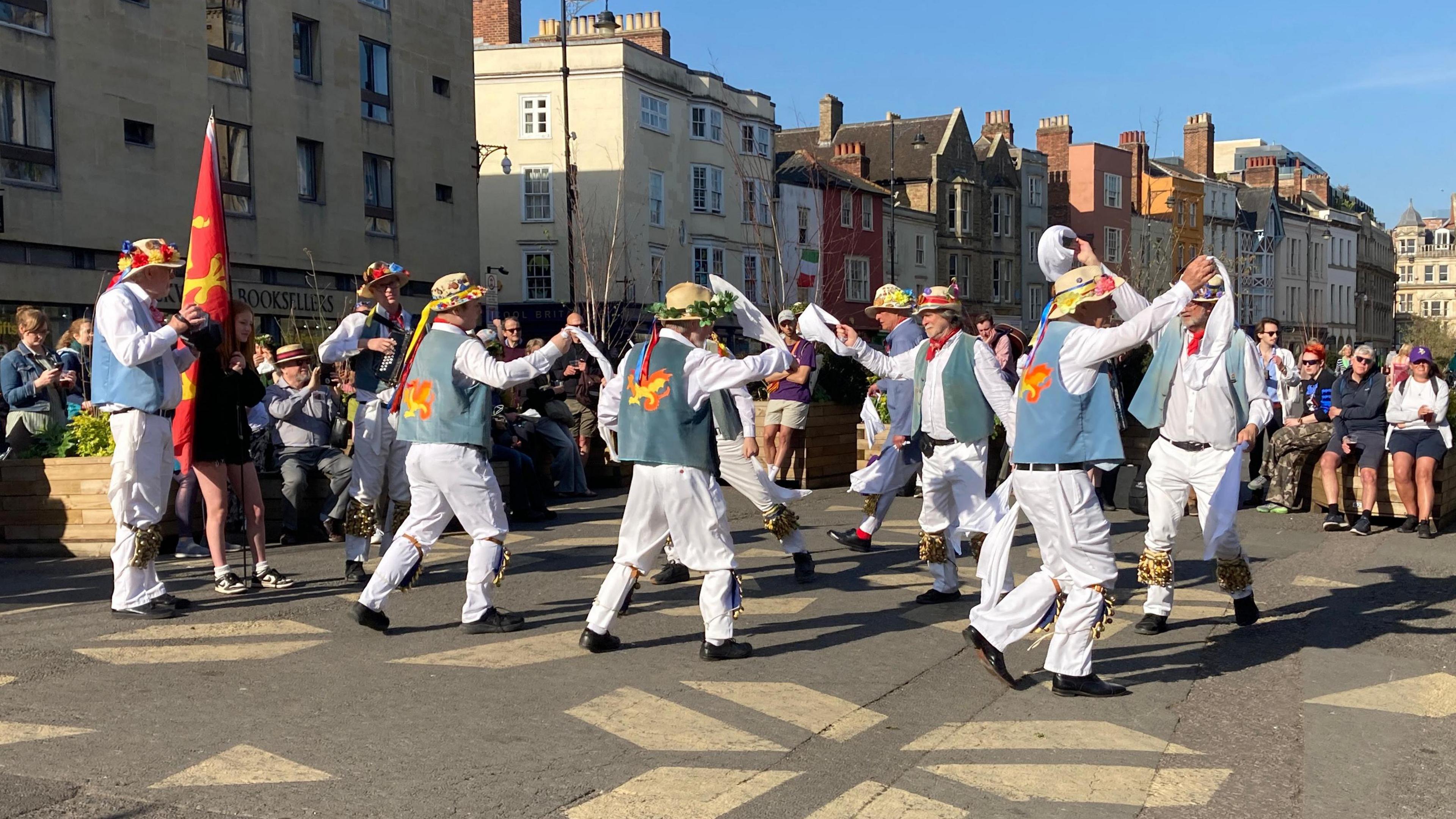 men in all white with blue waist coats morris dancing in the street in Oxford