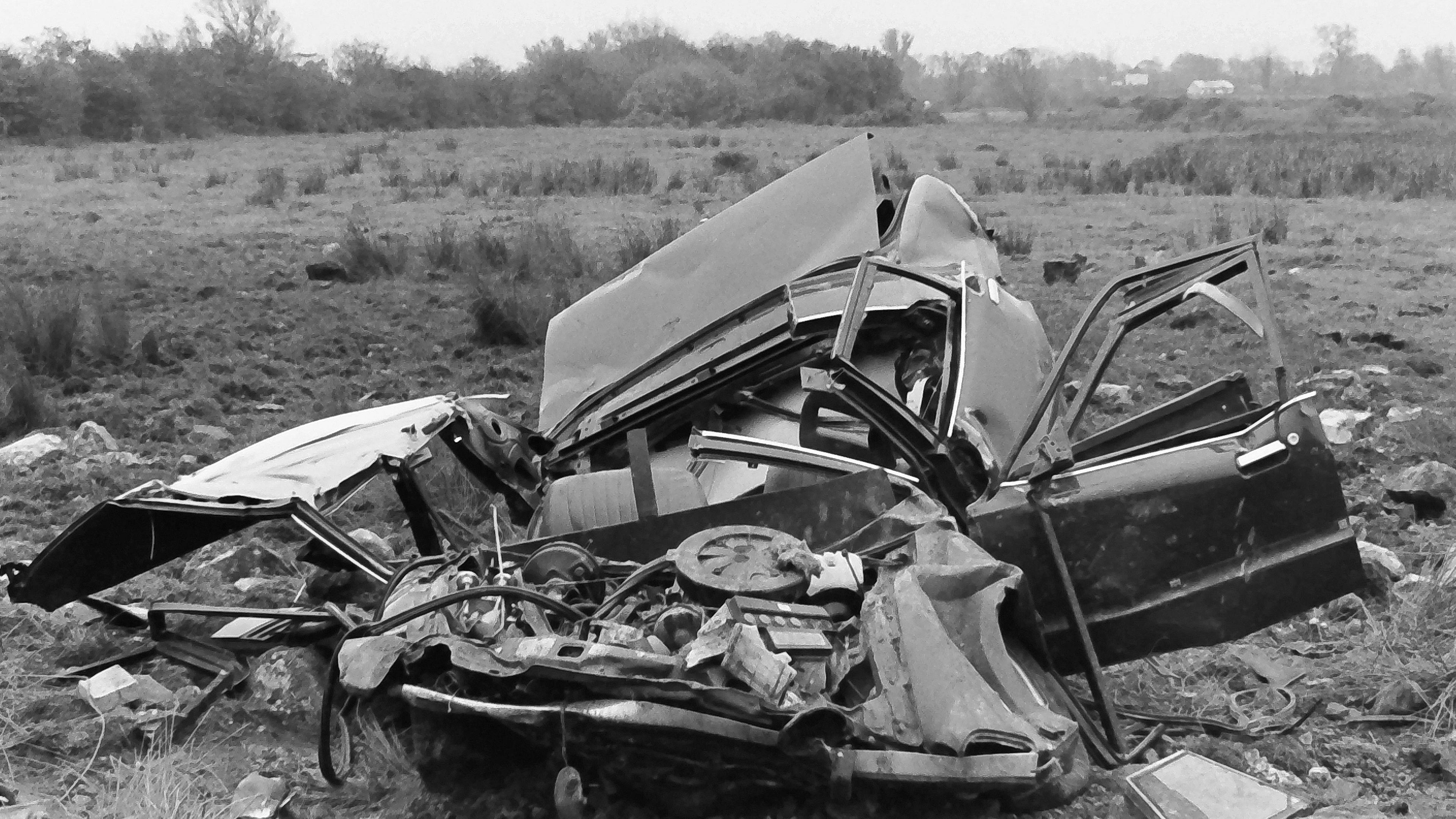 A black and white photo of the car that was blown up in the attack. The vehicle has been destroyed with its roof blown off and is lying in a field. Debris lies around the bomb site.