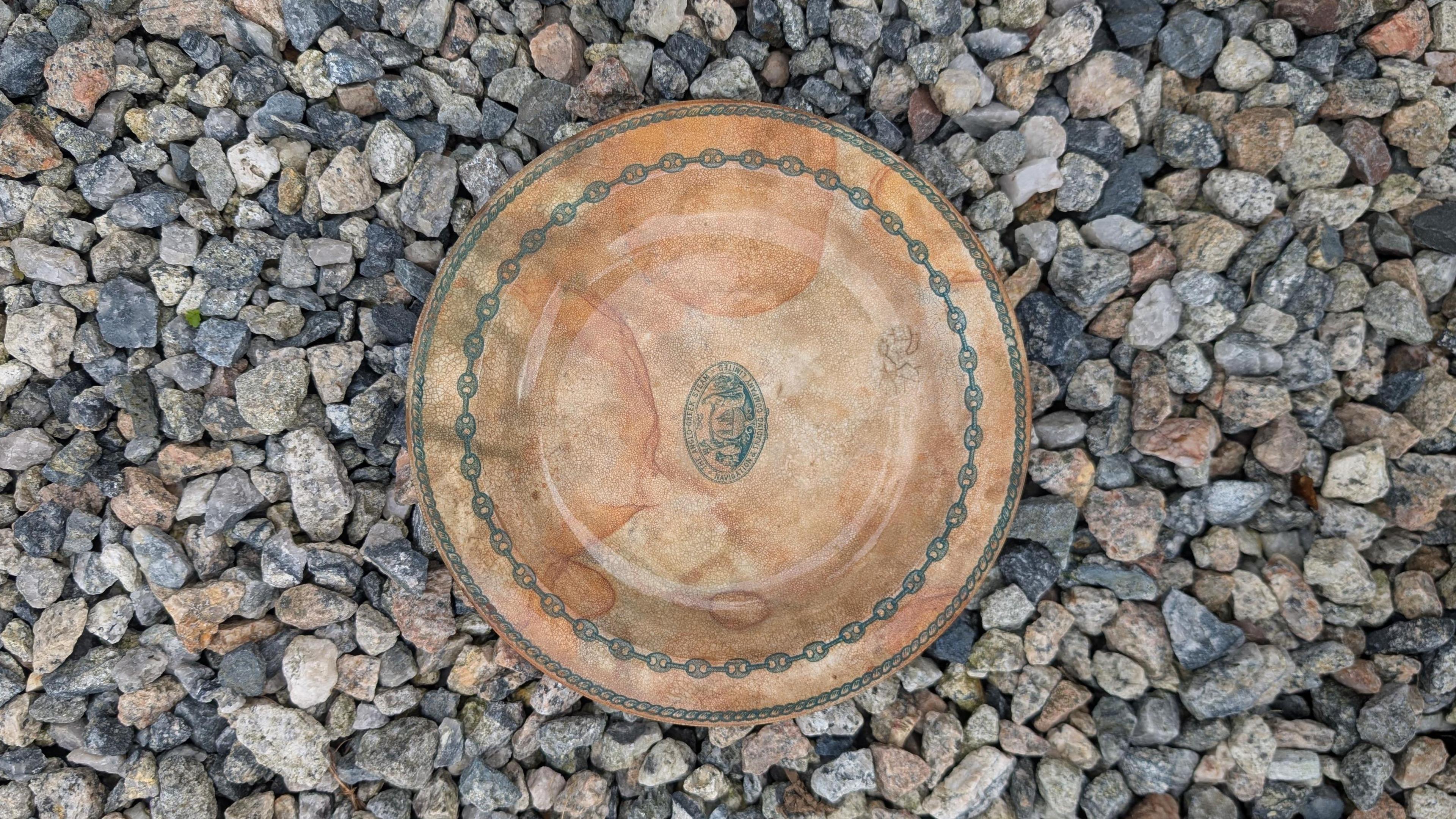 A picture of the crockery which is green and brown in colour. It is pictured in the middle of a number of stones on the floor.
