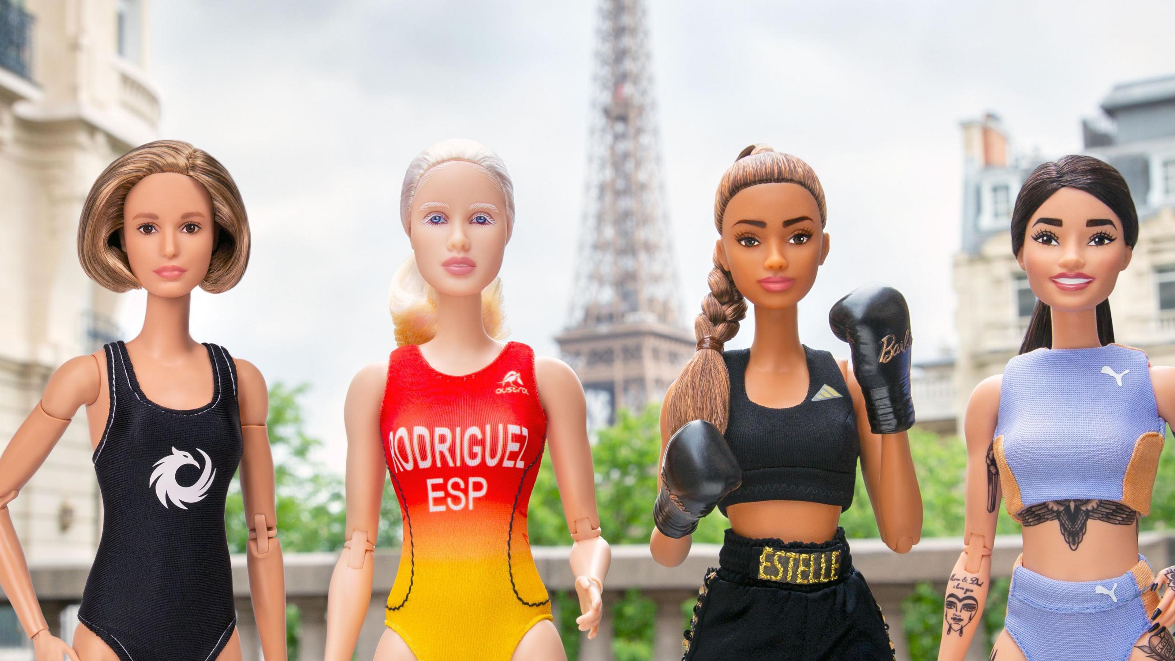 Four Barbie doll athletes in poses in front of the Eiffel Tower