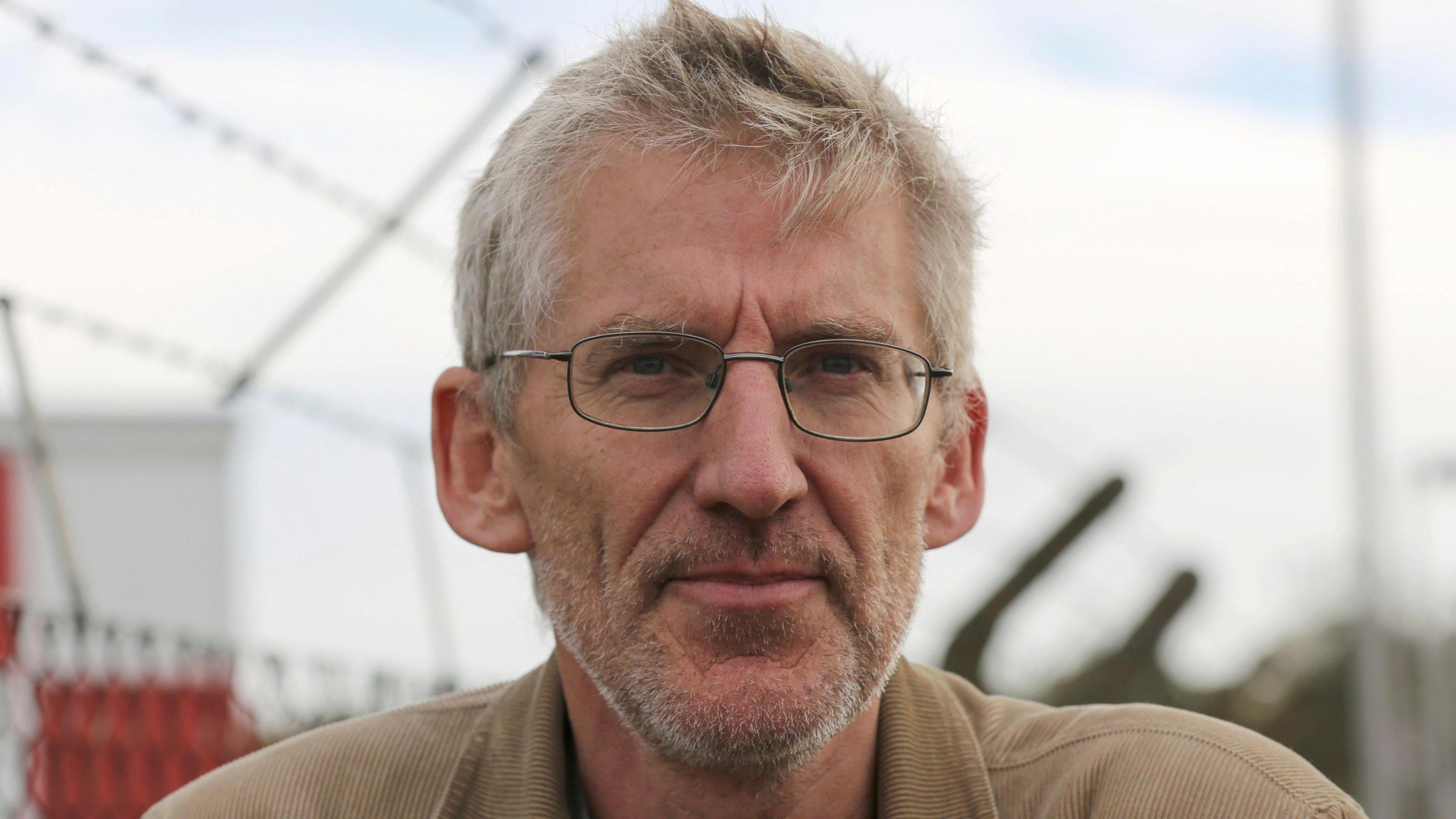 Clive Stafford Smith looking at the camera. He is wearing small metal-rimmed glasses and has short grey hair and a short beard