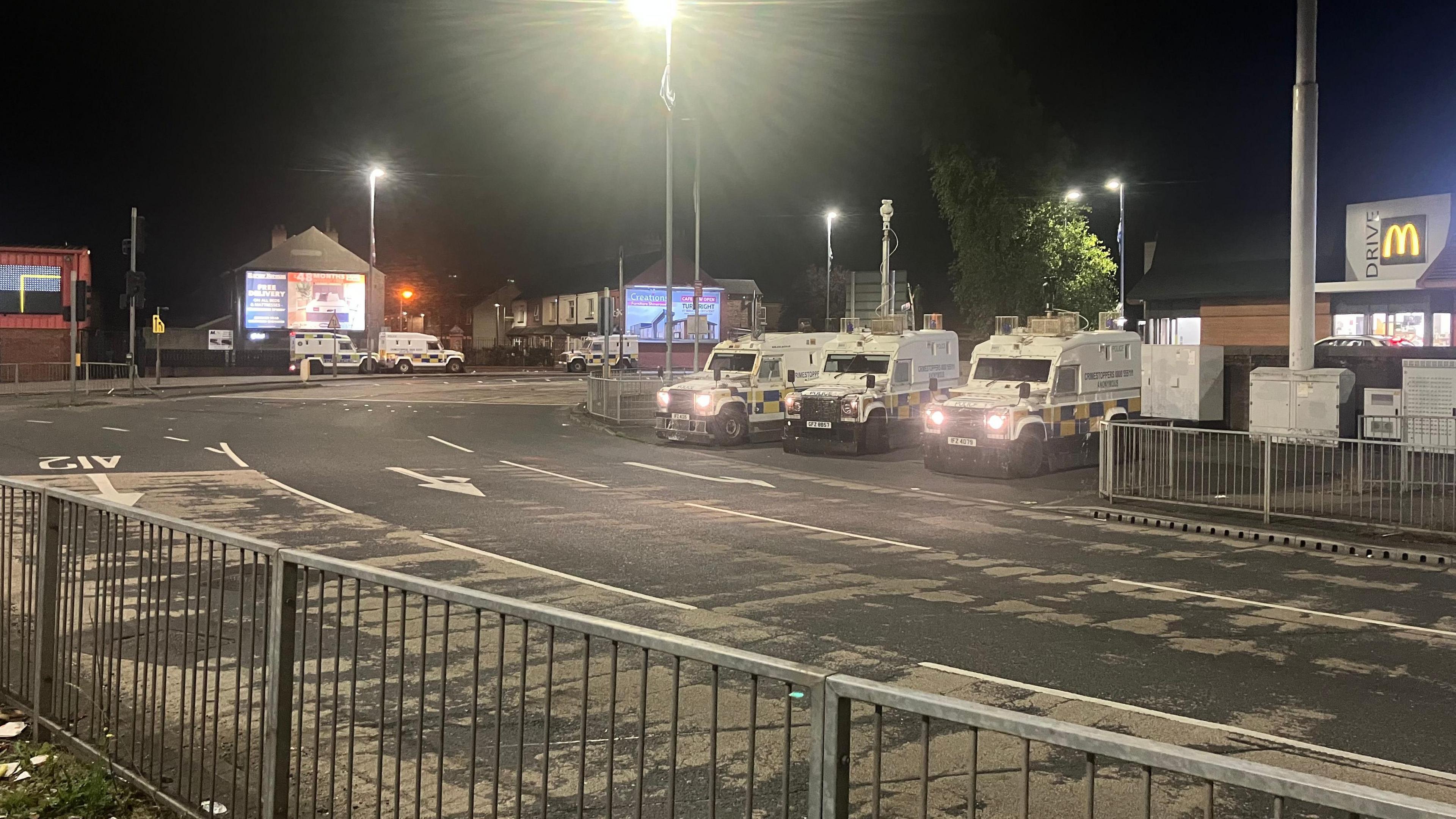 A wide shot of a street at Broadway Roundabout - three police Land Rovers are in the middle distance