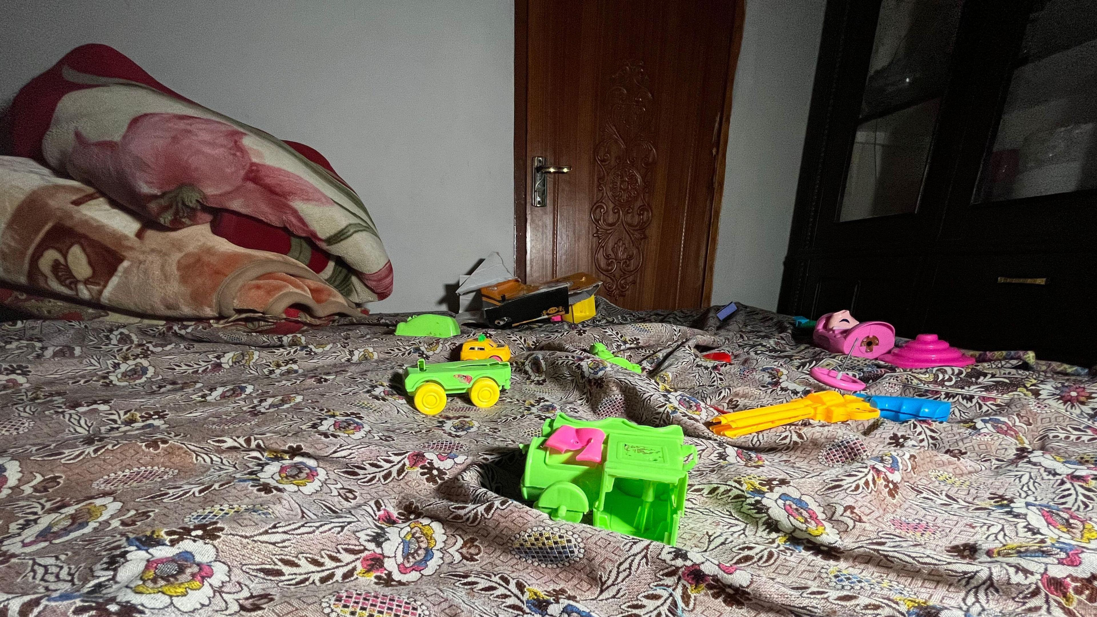 In a room at Muhammad Sharif’s house fluorescent toys lie scattered on a bed which has a patterned floral bedspread. A folded blanket is piled at one end of the bed.