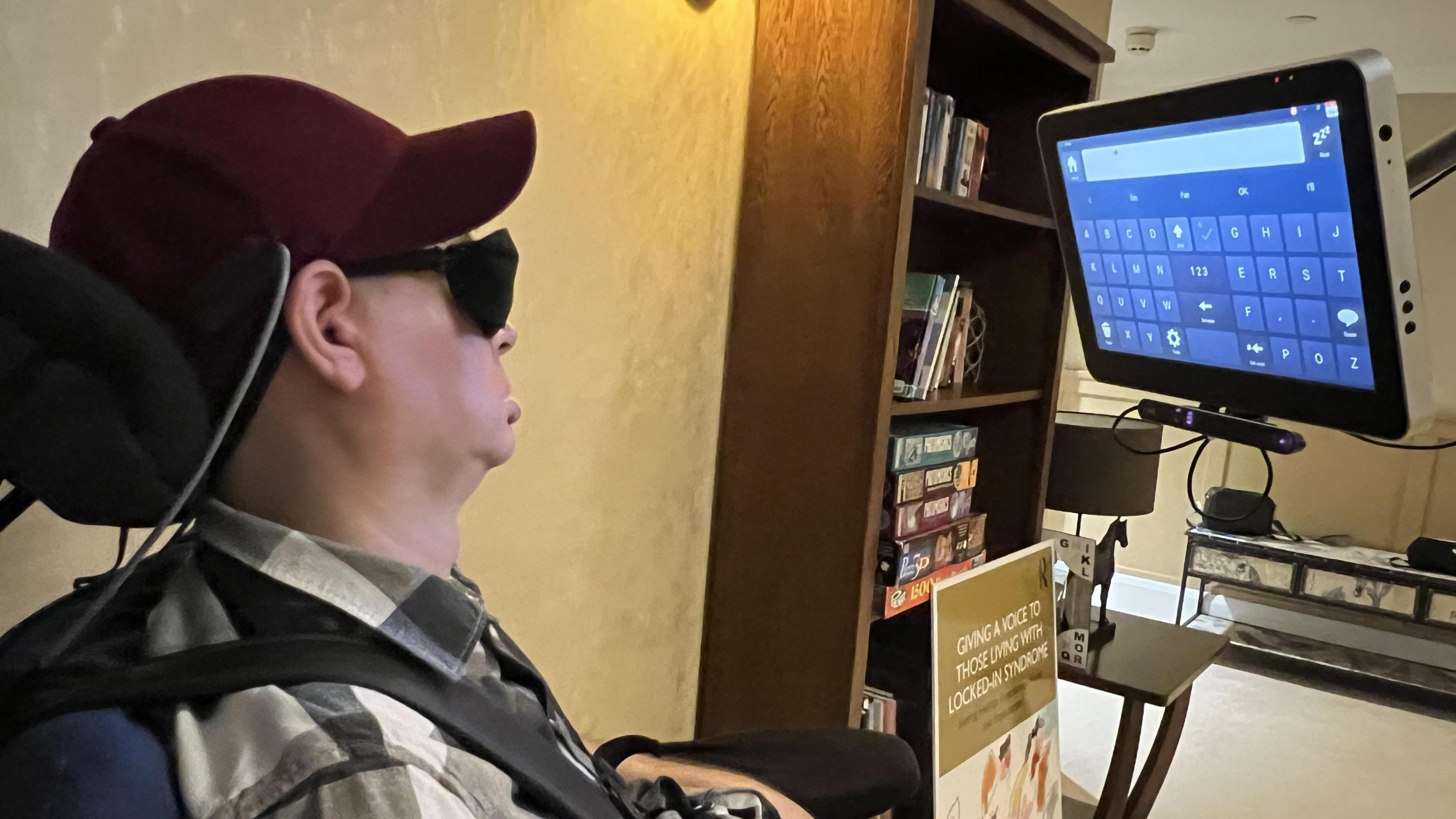 Bram Harrison in his wheelchair, in front of an eye-controlled computer screen with boxes which can be controlled with the gaze of his left eye.