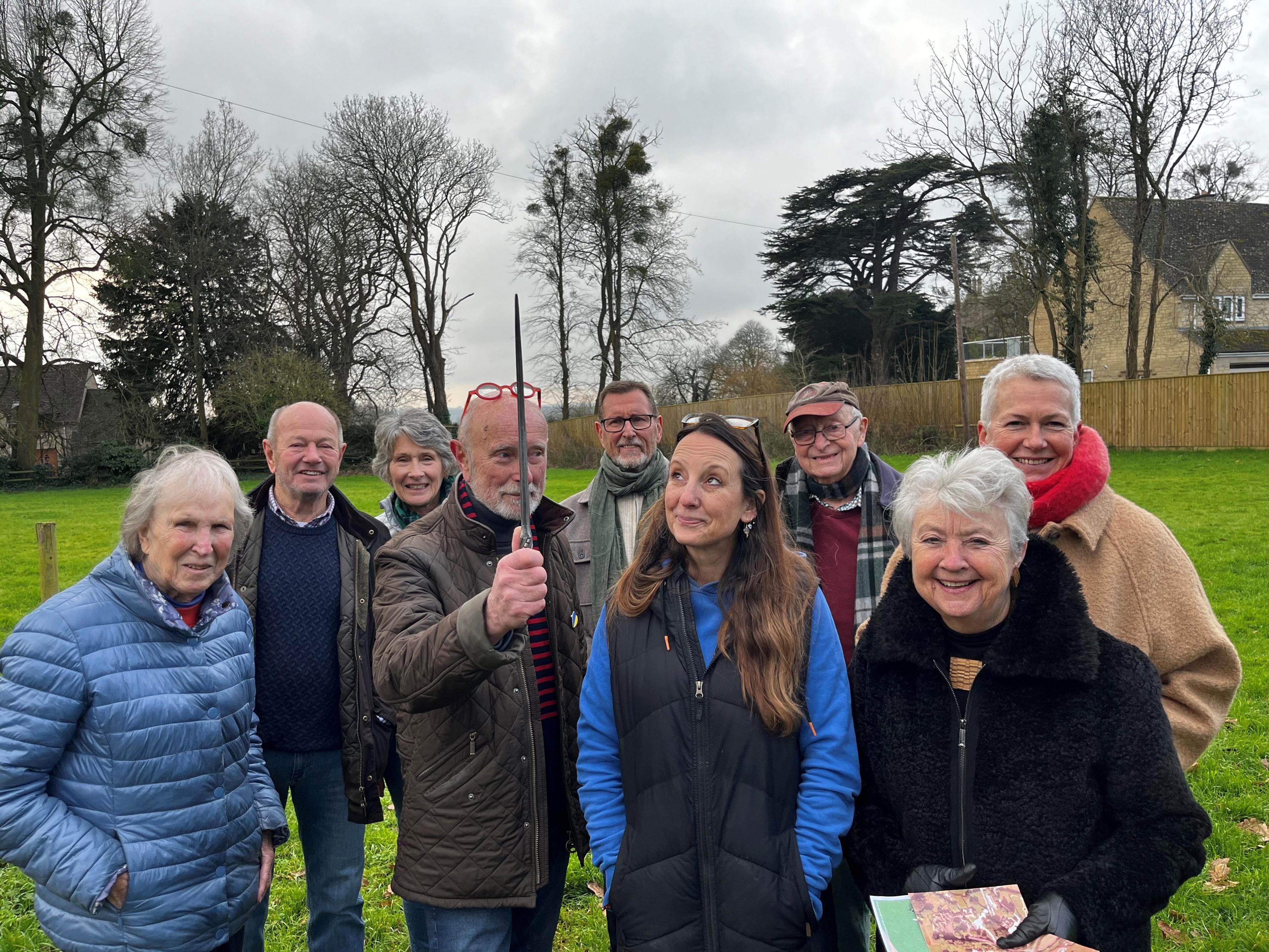 A group of nine people standing grouped together in two lines on a field.  They are all smiling and wrapped up in warm clothes.