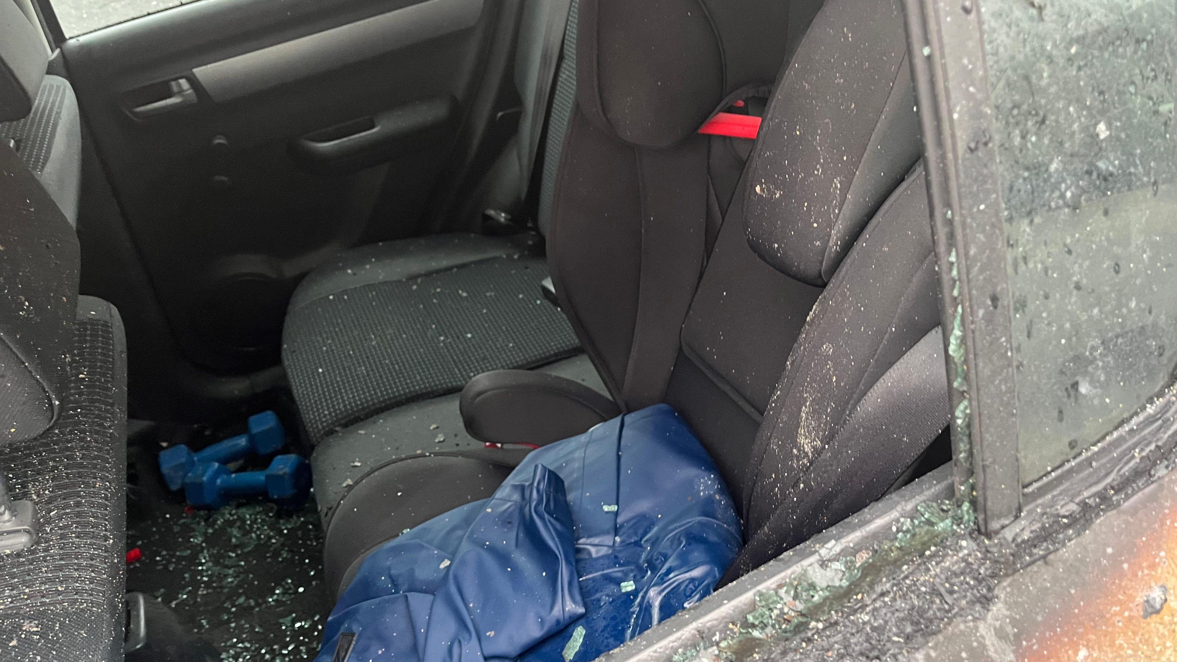 A broken backseat car window; the seats are black, and there is glass over the floor. 