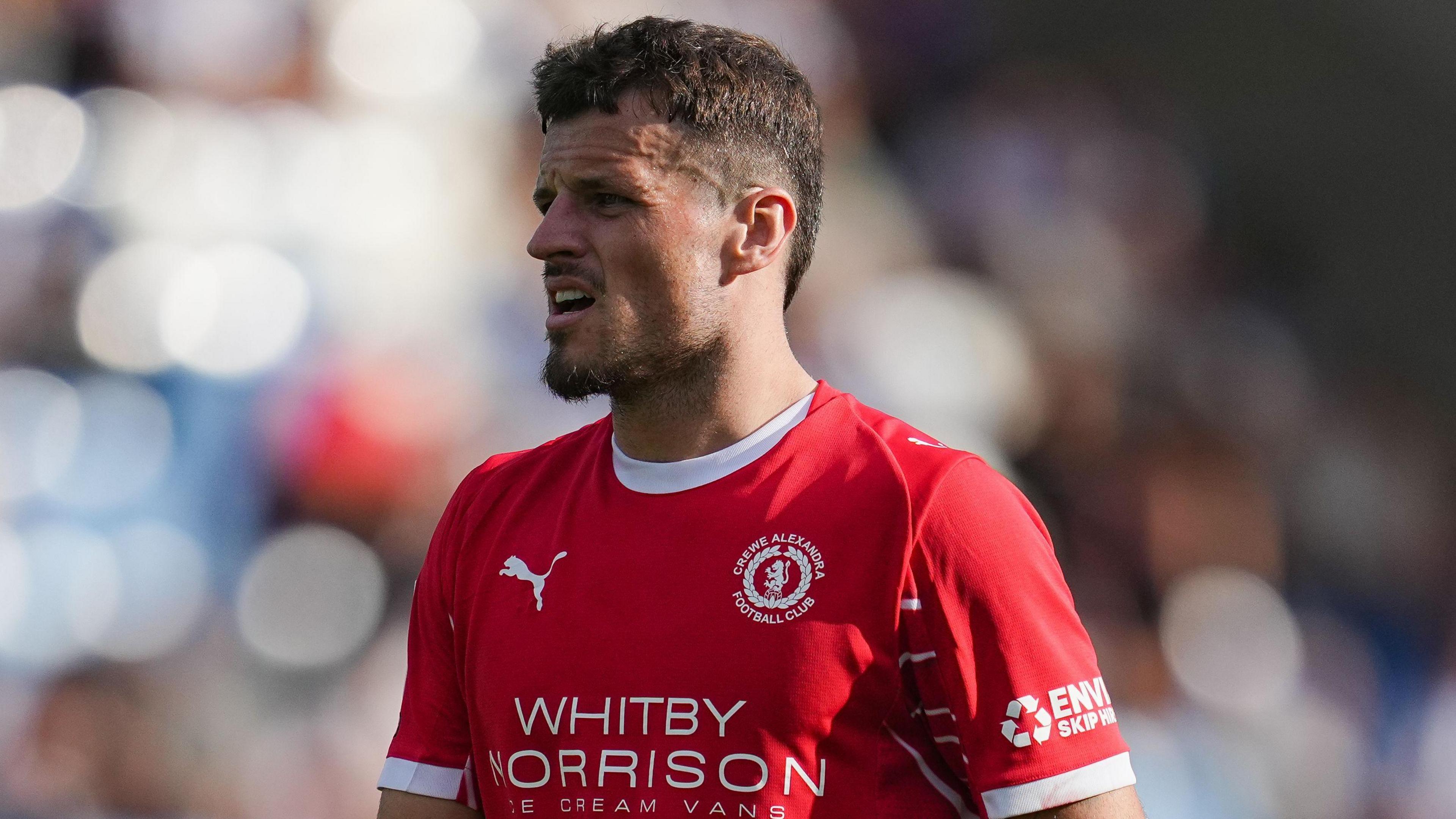 Crewe striker Josh March looks to his right during a match. He is wearing a red Crewe home shirt.