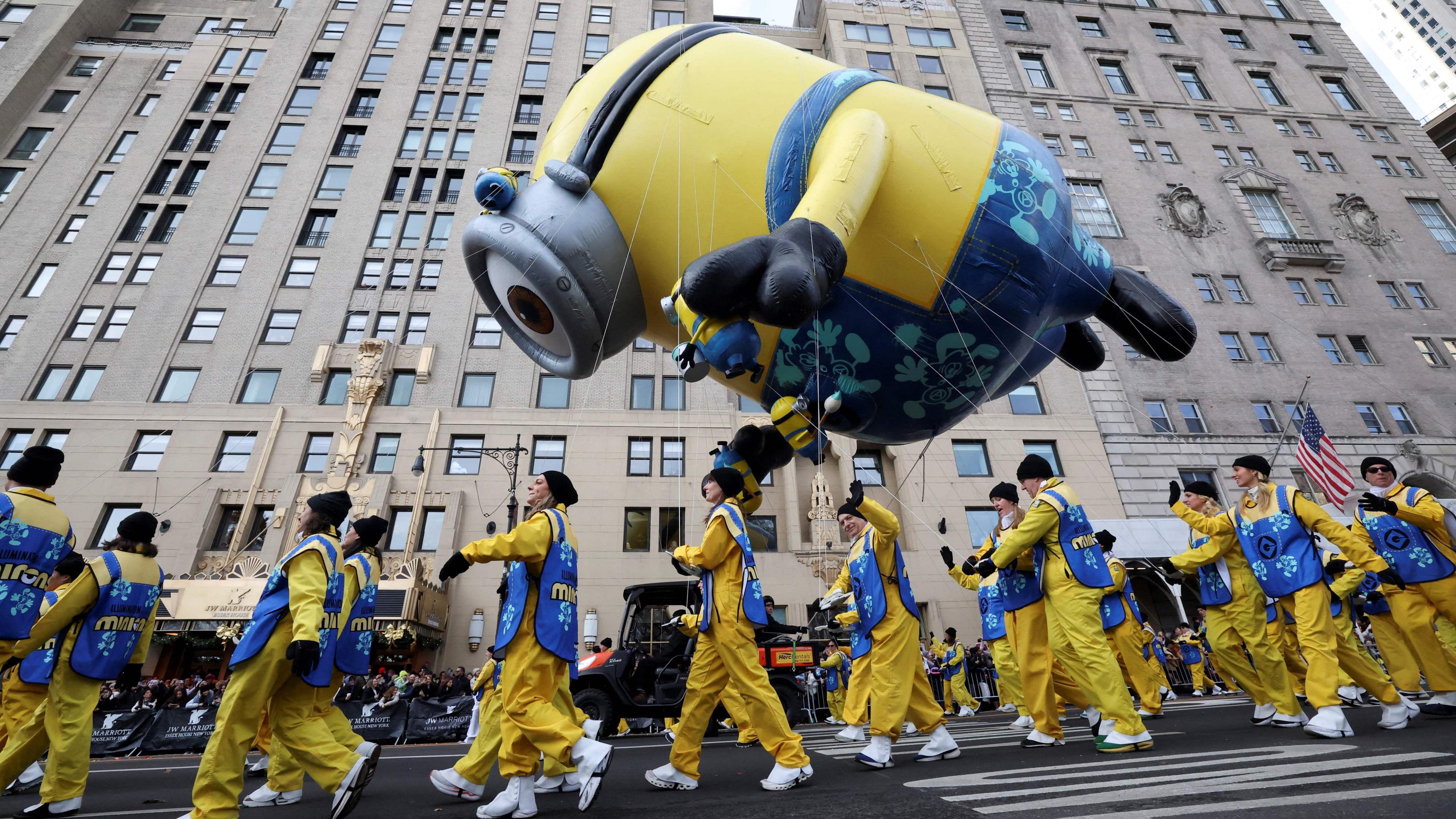 A minion balloon is carried by people wearing yellow with blue tabards through the streets of New York.