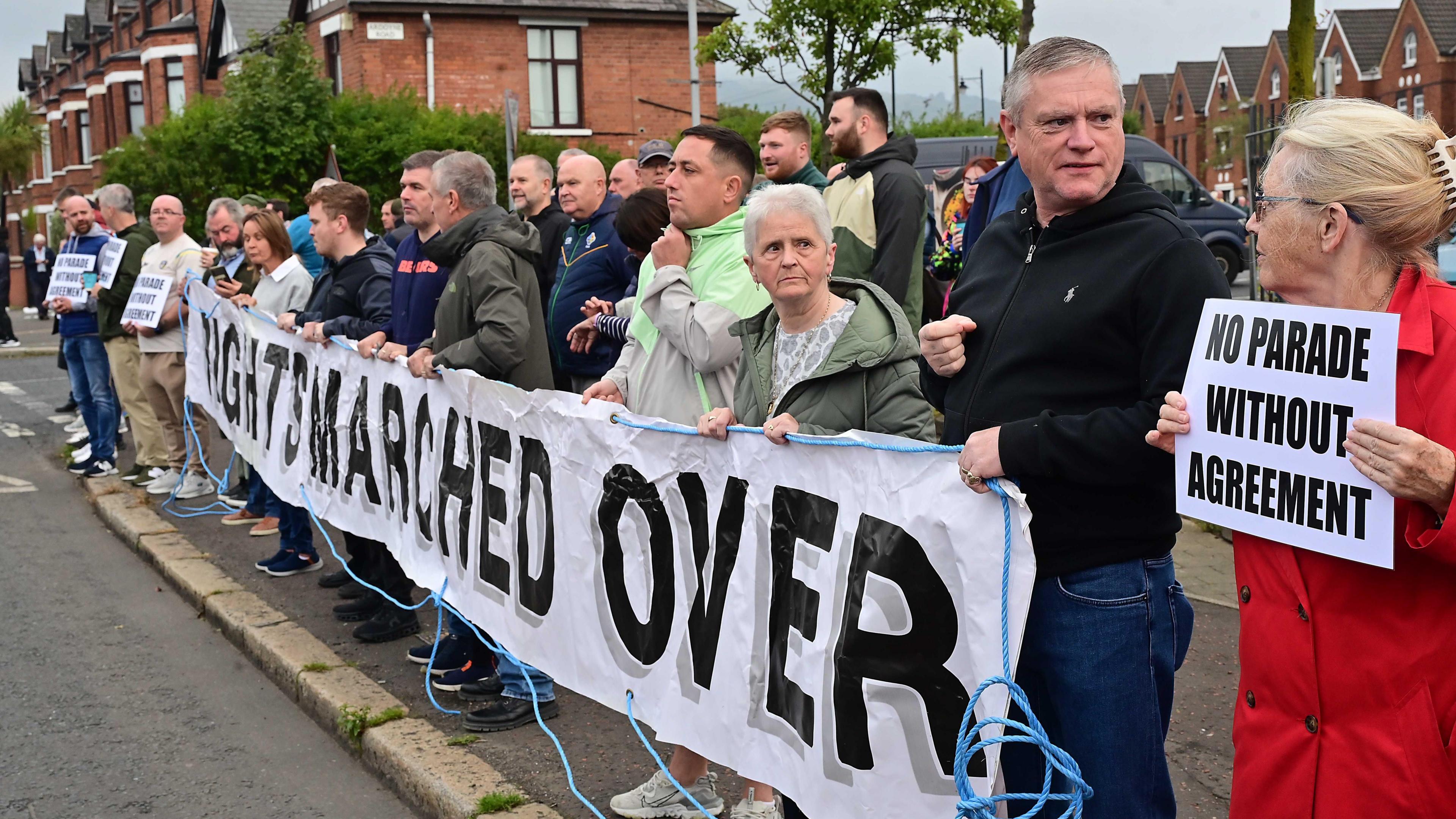 Roadside scene showing more than a dozen people behind a sign which reads 'rights marched over'