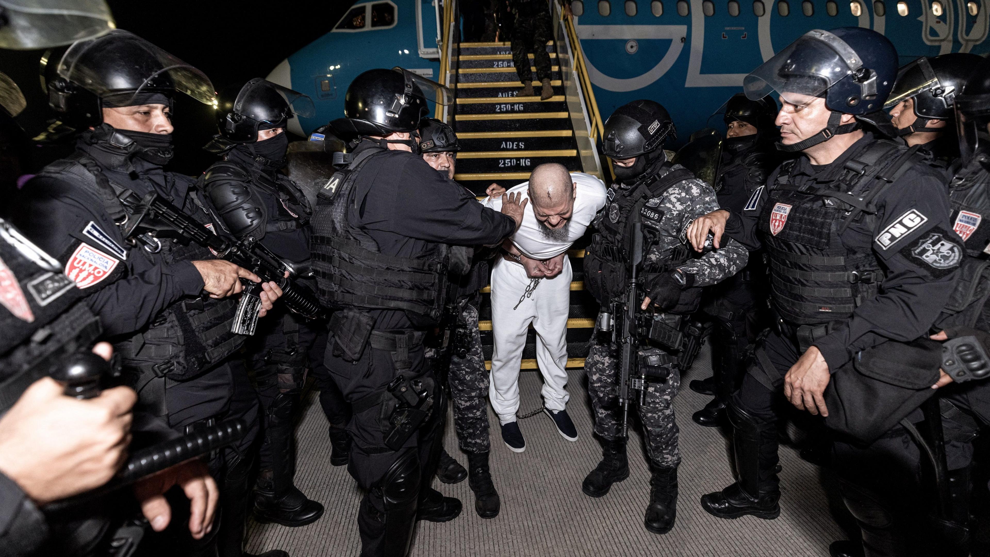 Salvadoran police officers escort detainees from a plane on the tarmac at the El Salvador International Airport in San Luis Talpa.