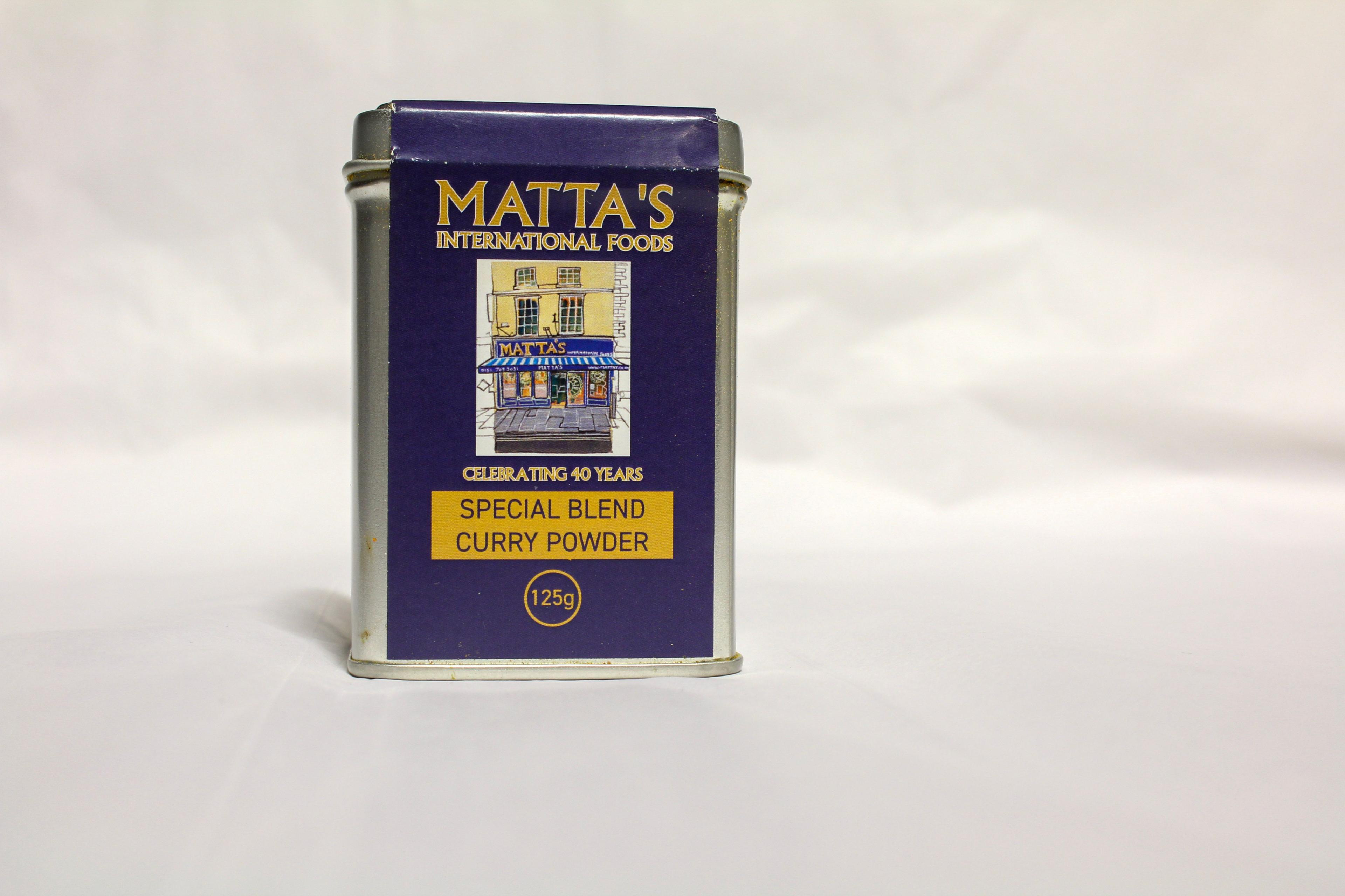 A small rectangular tin, with a navy sticker on the front, with yellow writing which reads 'Matta's International Foods celebrating 40 years, special blend curry powder'.