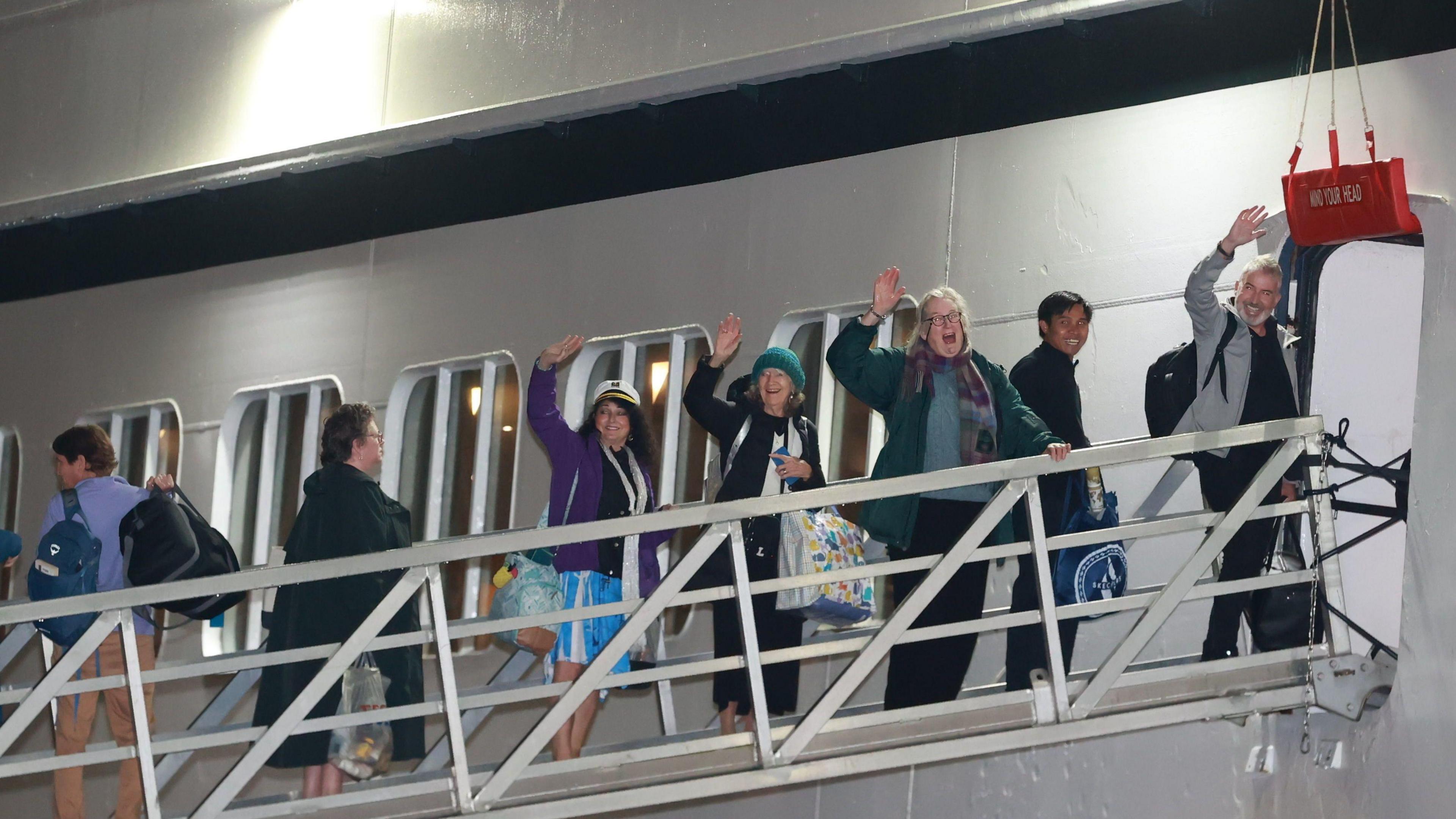 Seven passengers boarding the ship from a platform. Four of them are waving.