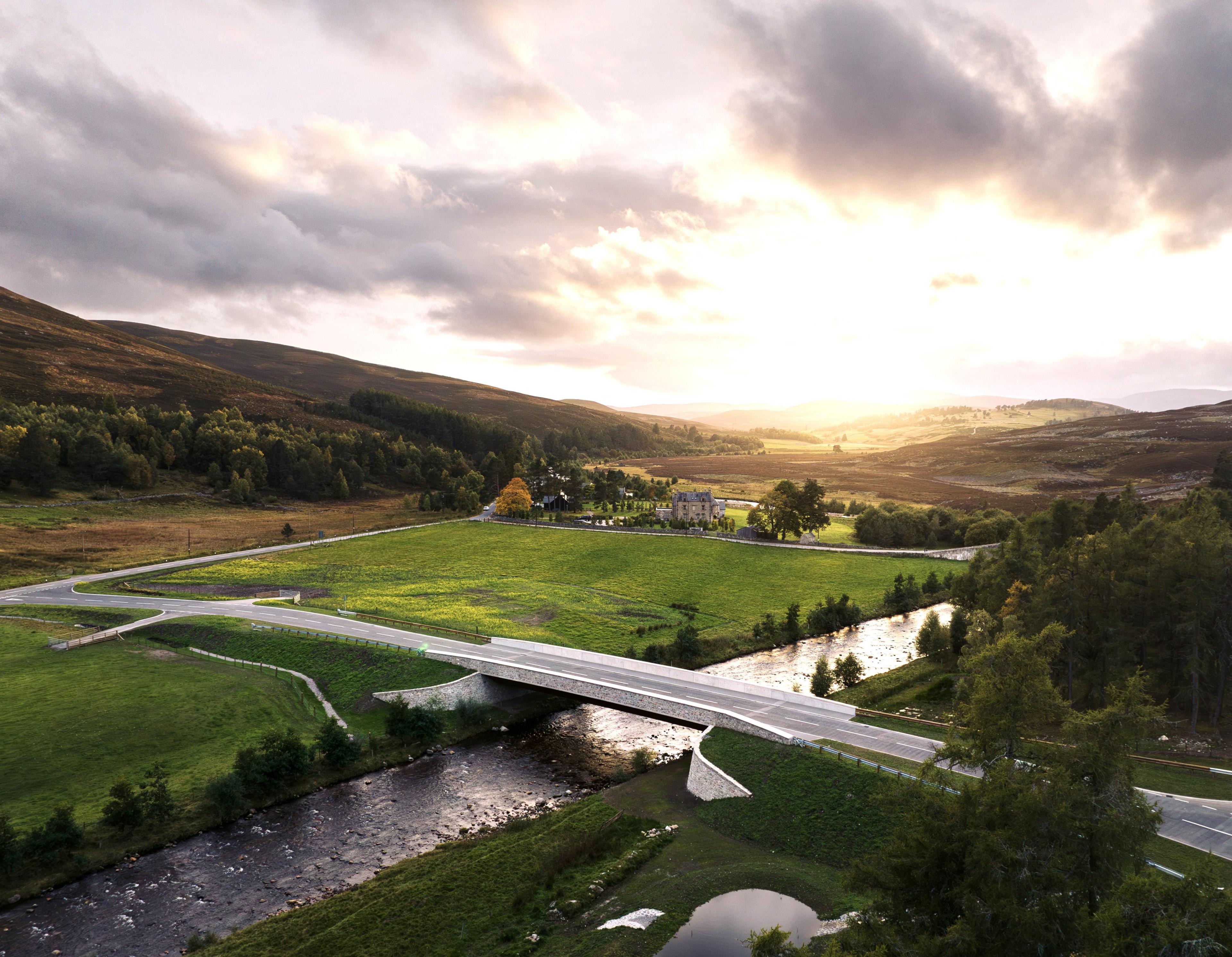 Drone image of Gairnshiel Jubilee Bridge taken as the sun starts to set. It looks clean and neat set in perfect green grassy surroundings, the hills rilling into the distance and a large house sitting in the background.
