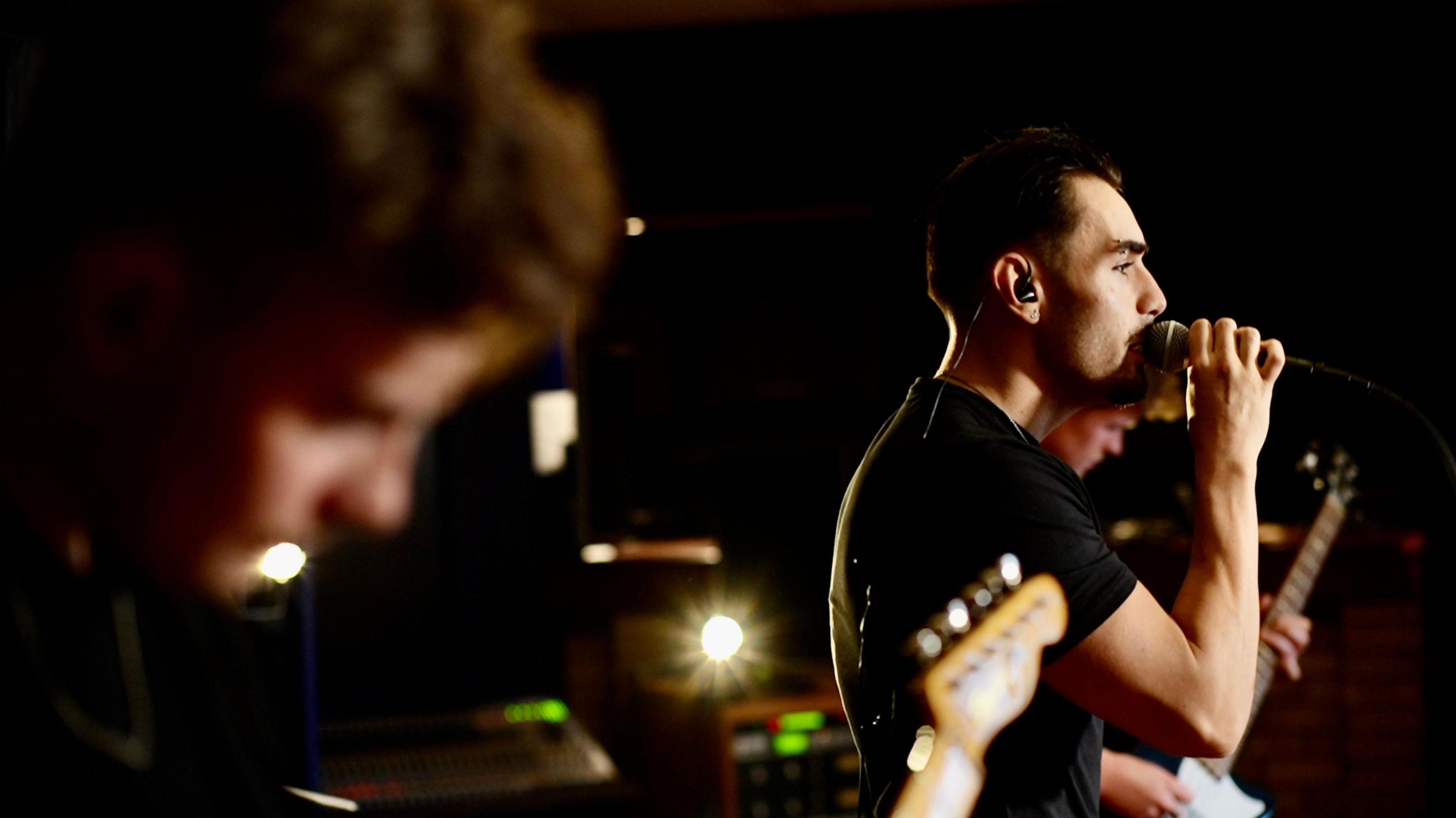 Ben Watts in focus, as he sings into the microphone, whilst Luke Ellis is out of focus in the forefront of the image.