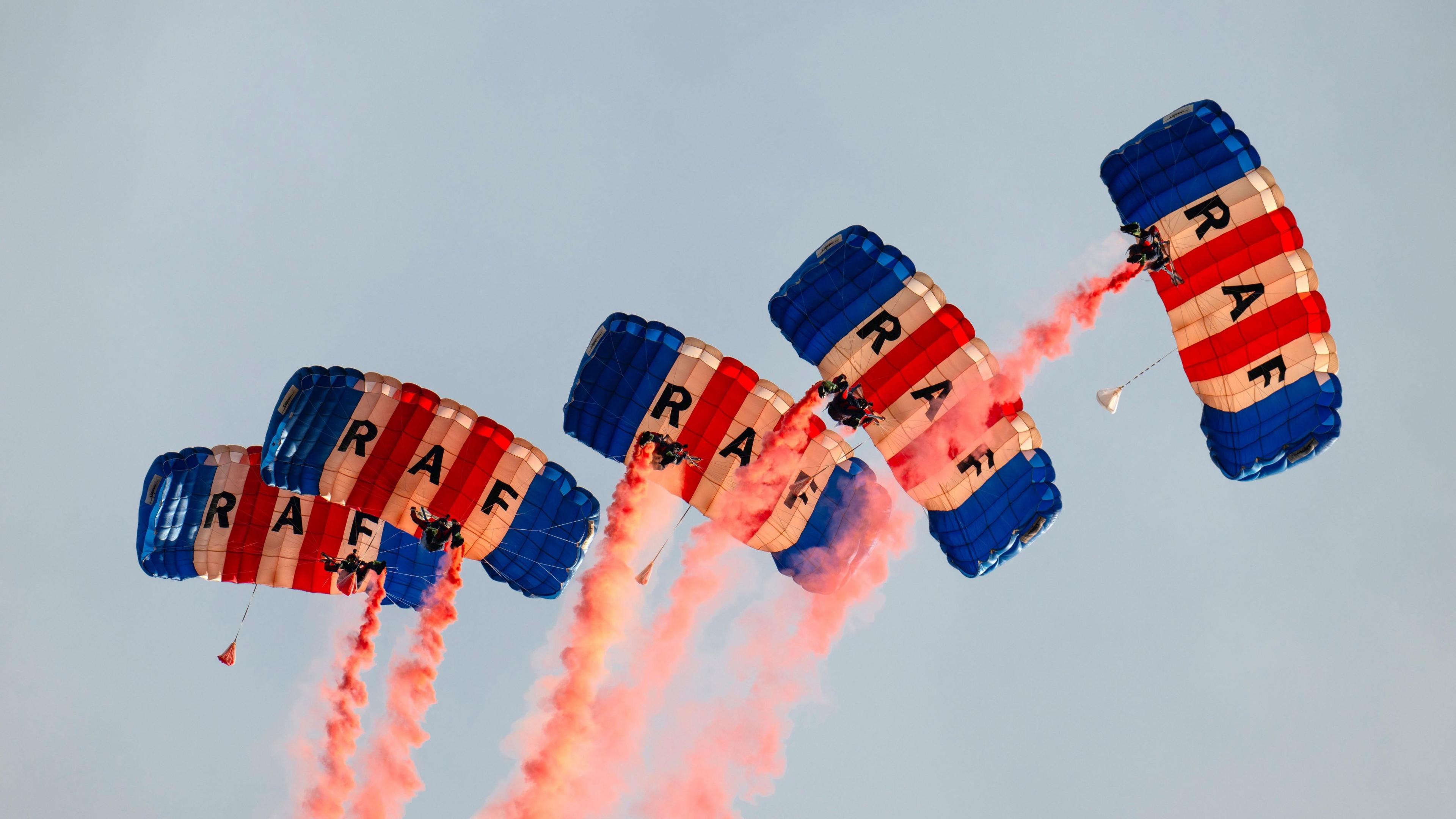 RAF parachutists with blue red and white parachutes with red smoke trailing across the sky