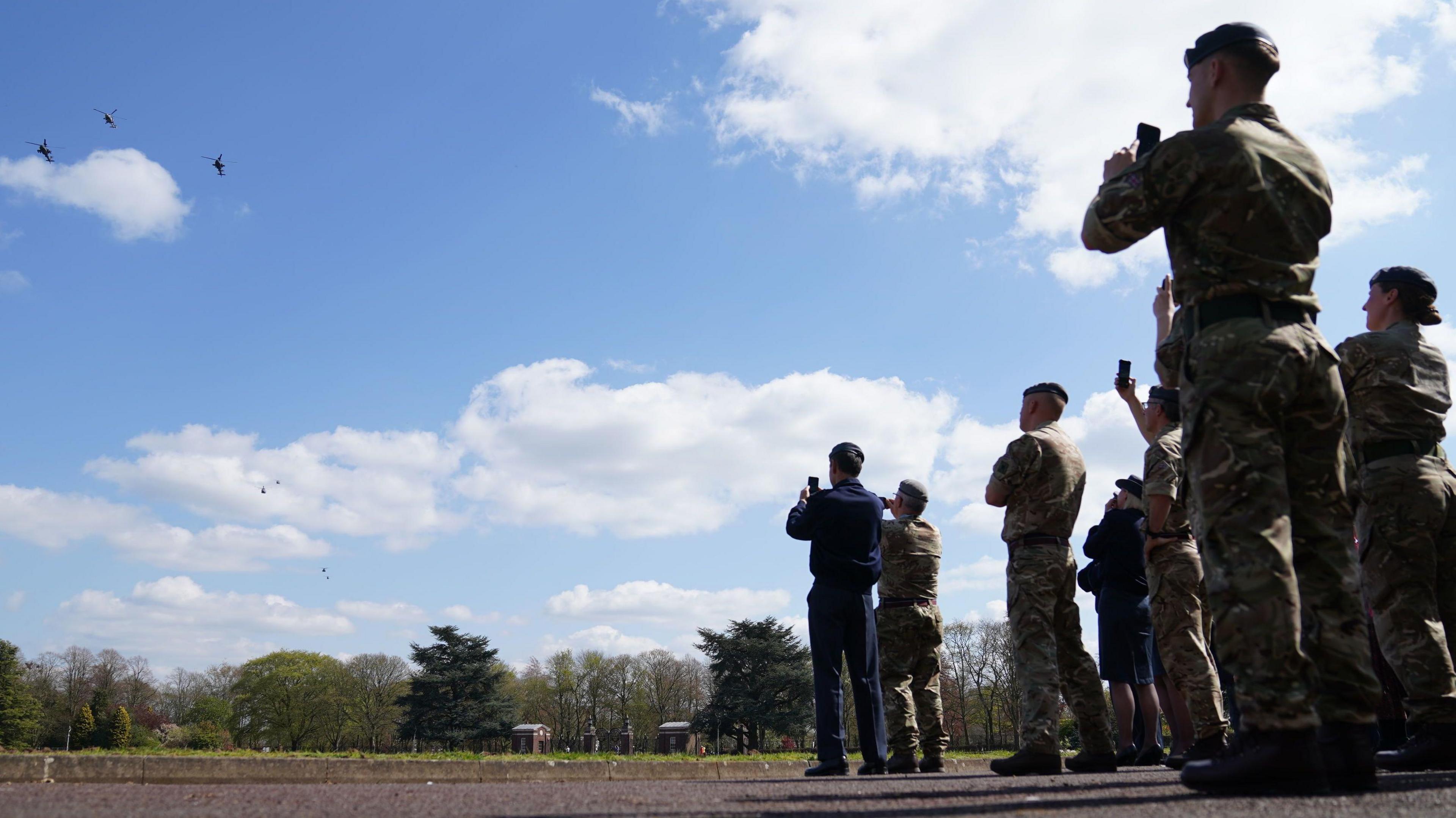 Military staff watch helicopters practise a formation