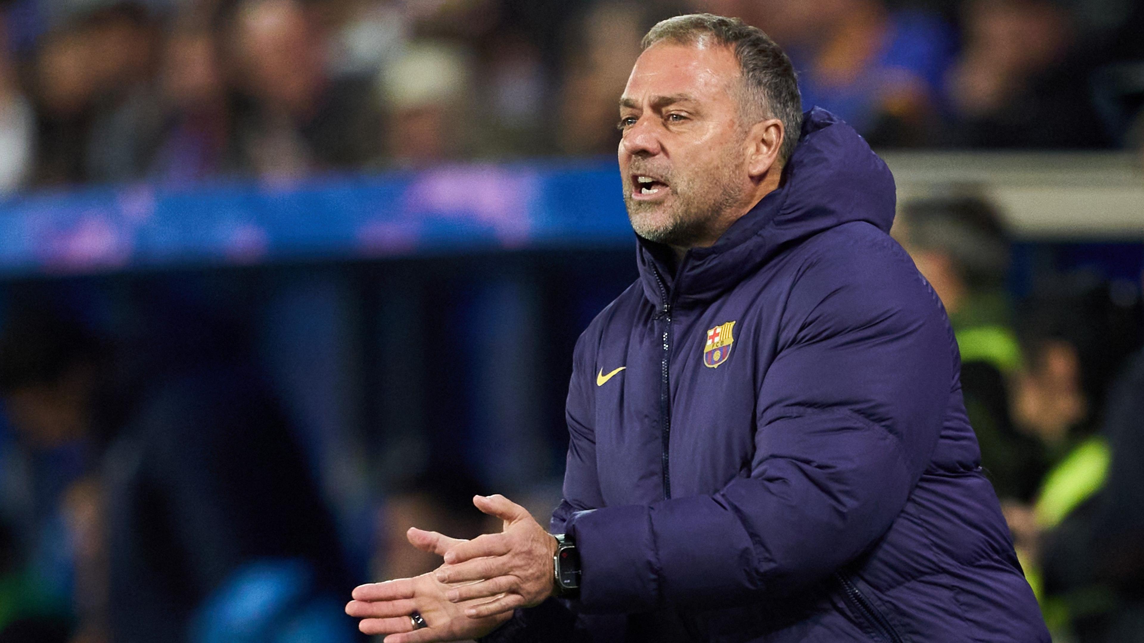 Hansi Flick, wearing a blue padded Barcelona club coat, stands in the touchline, applauding