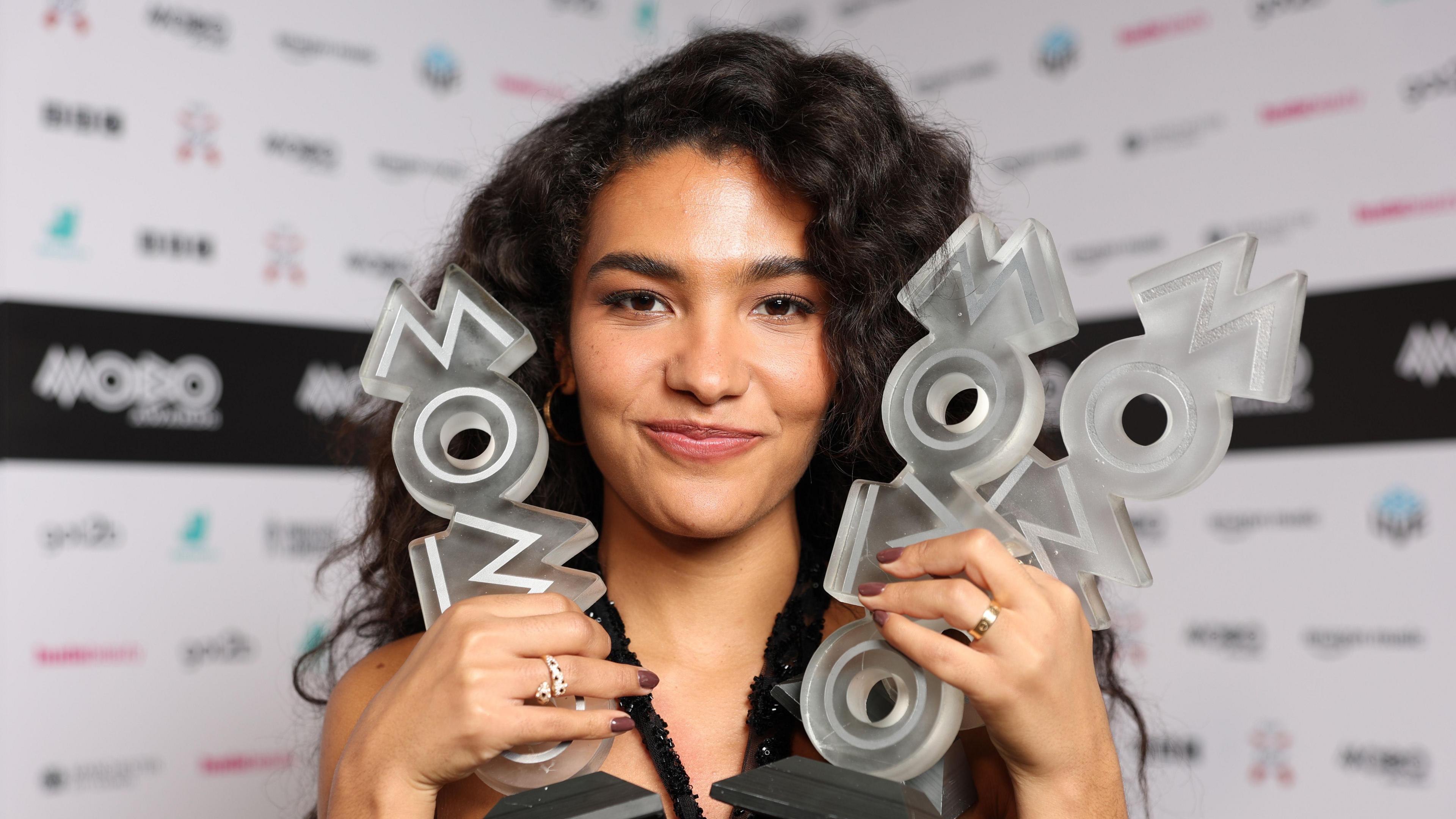 Olivia Dean holding three Mobo trophies