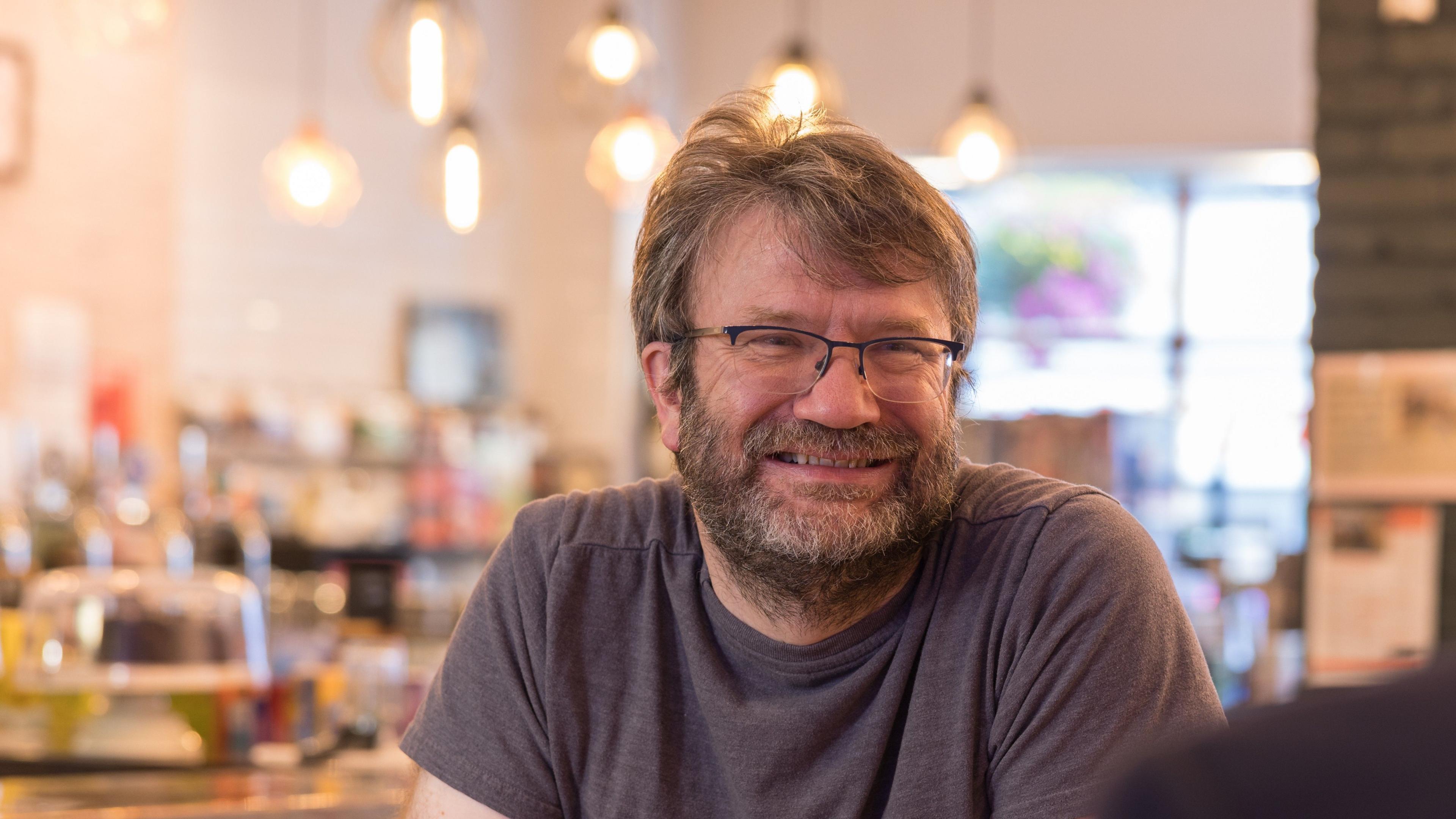 Nick Smith, who runs the Ludoquist board game cafe, sitting in his cafe, smiling at someone off camera