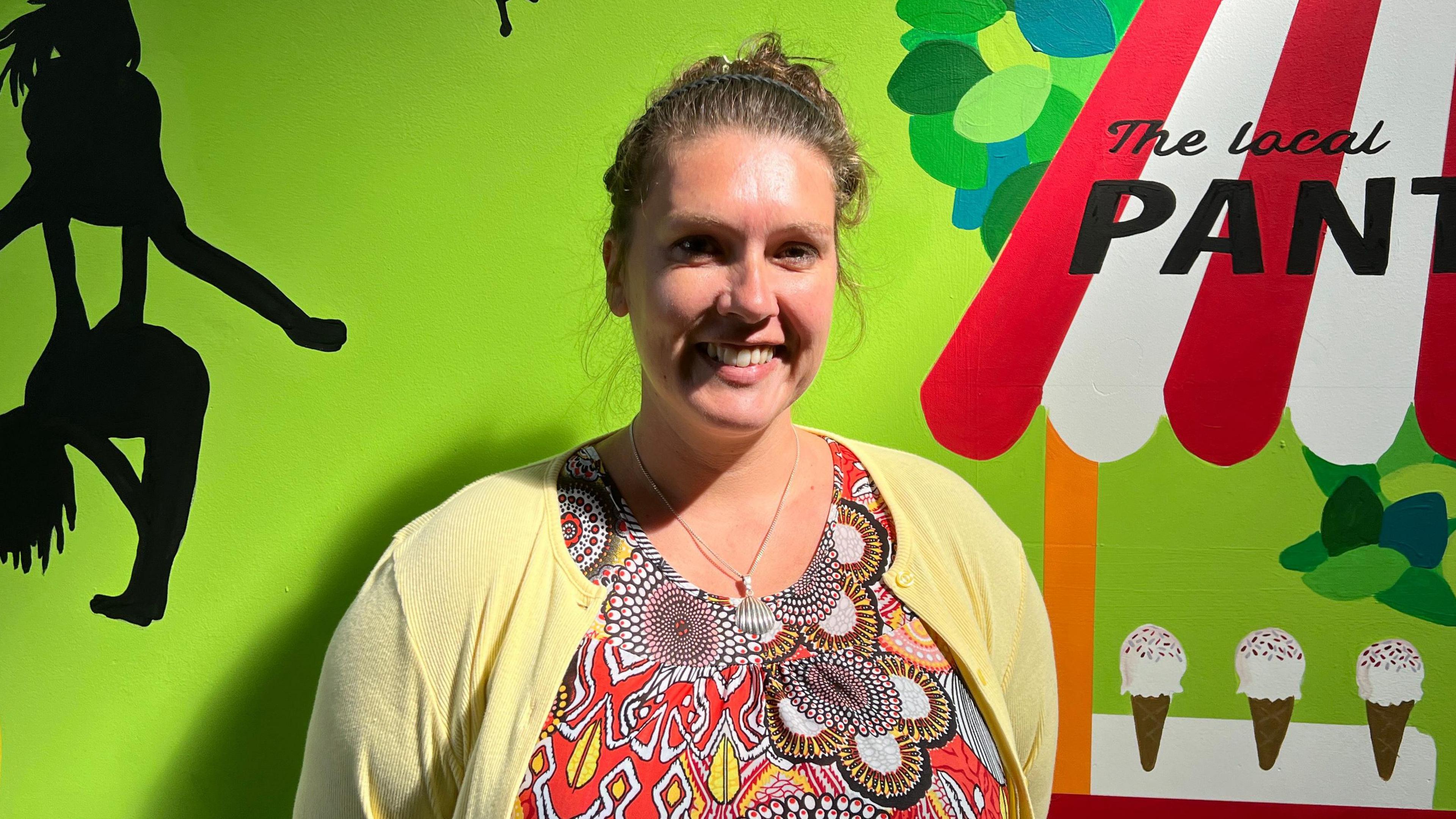 Laura Fowler in a colourful top standing in front of a painted wall