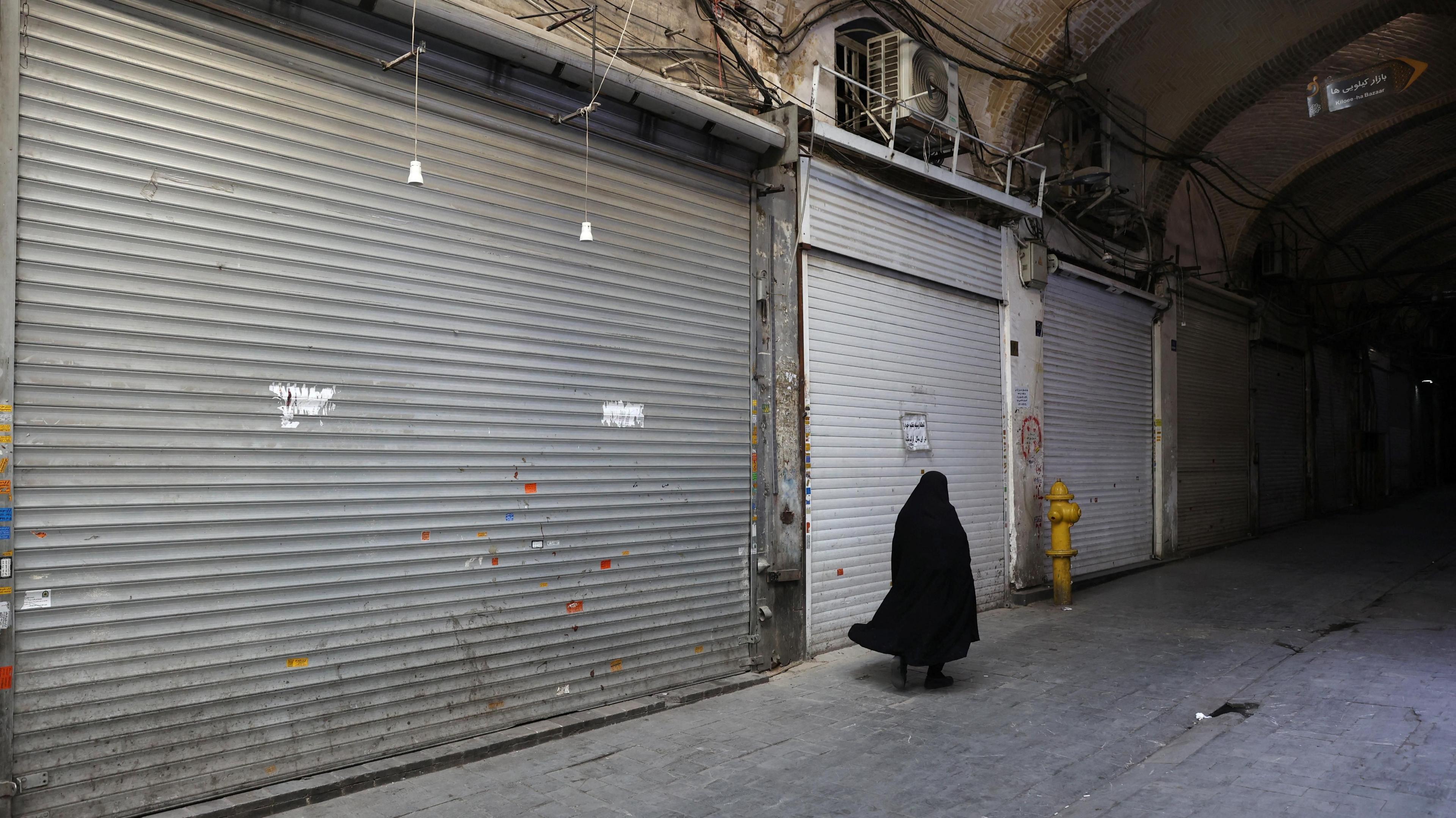 A woman walks past shuttered shops at Tehran's Grand Bazaar (16 June 2025)