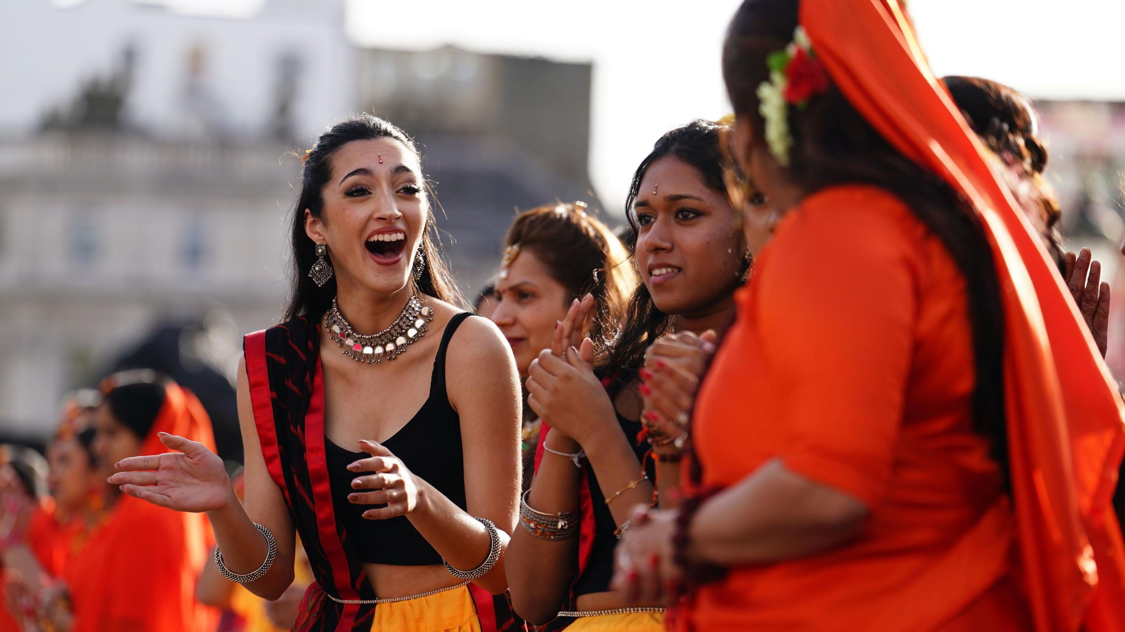 Women performers in black and orange clothing clap and chat in Trafalgar Square