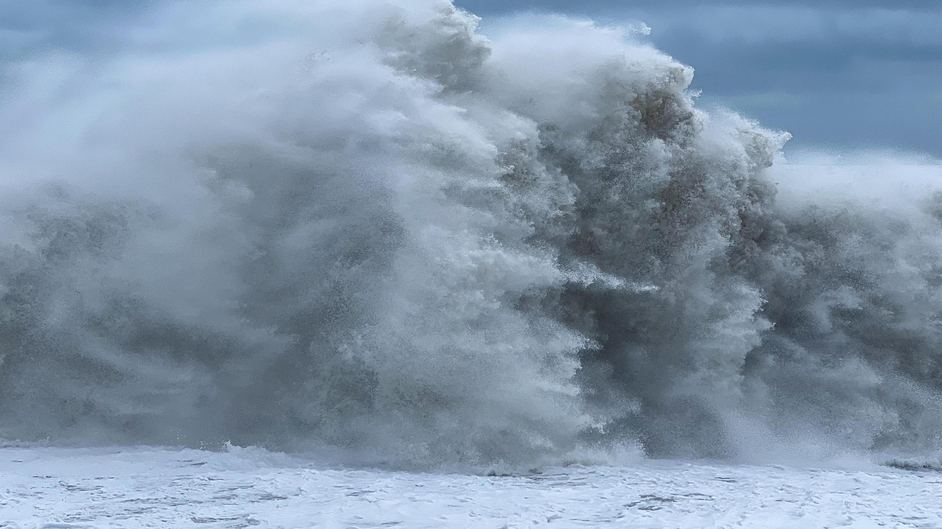 A giant white wave at sea with stormy grey skies in background