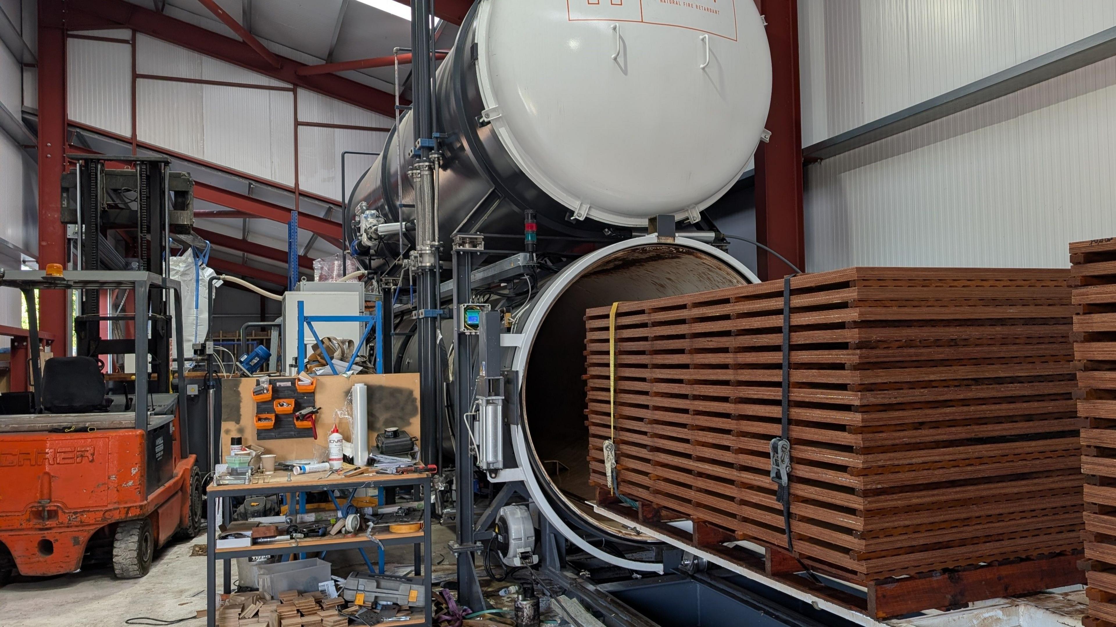 A neat bundle of wood being moved into a large cylinder, where it will be exposed to a vacuum and pressure. 