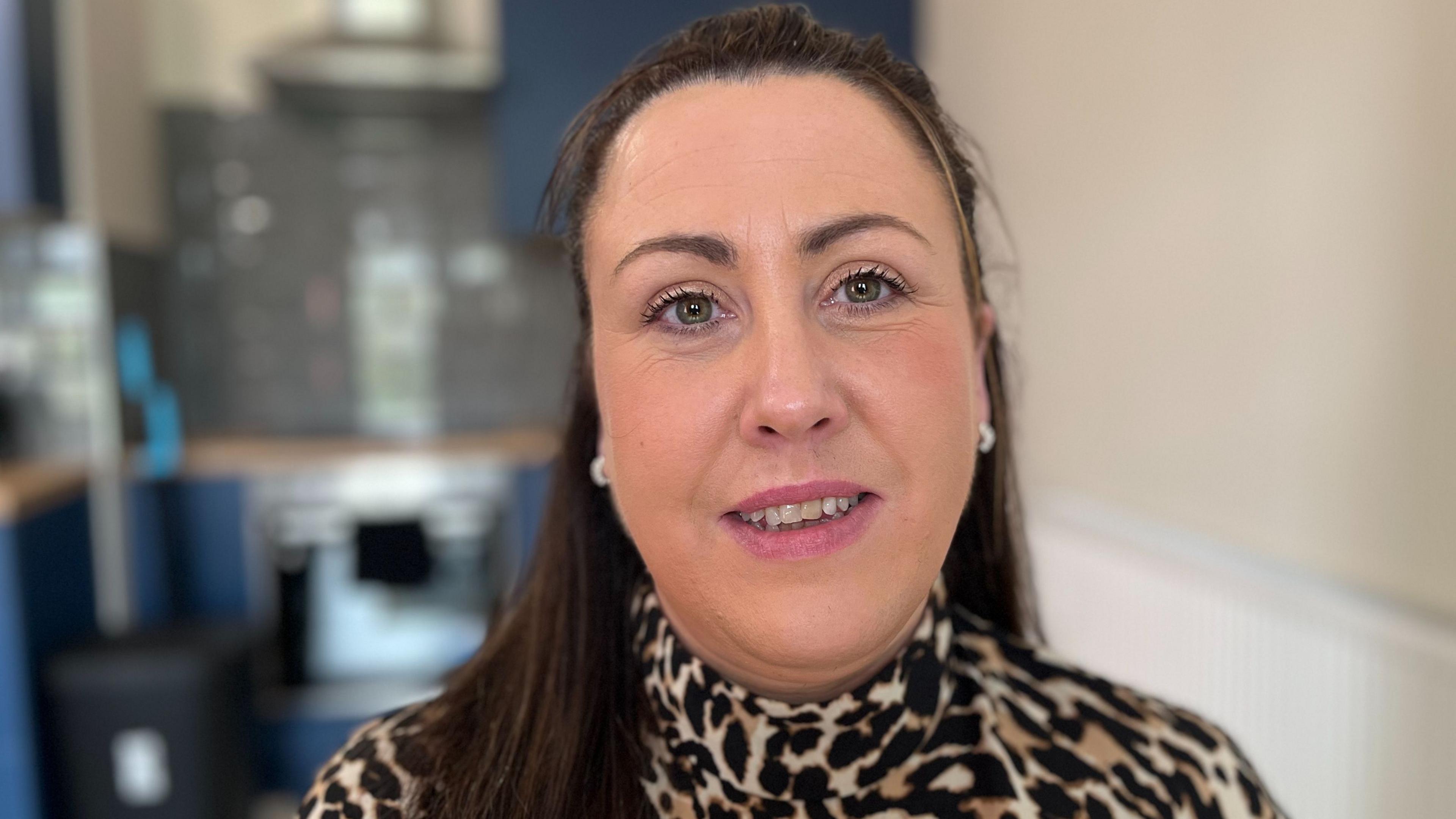 Fiona Boyd sits in the office and looks at the camera with a slight smile on her face. She has long brown hair and a leopard print top