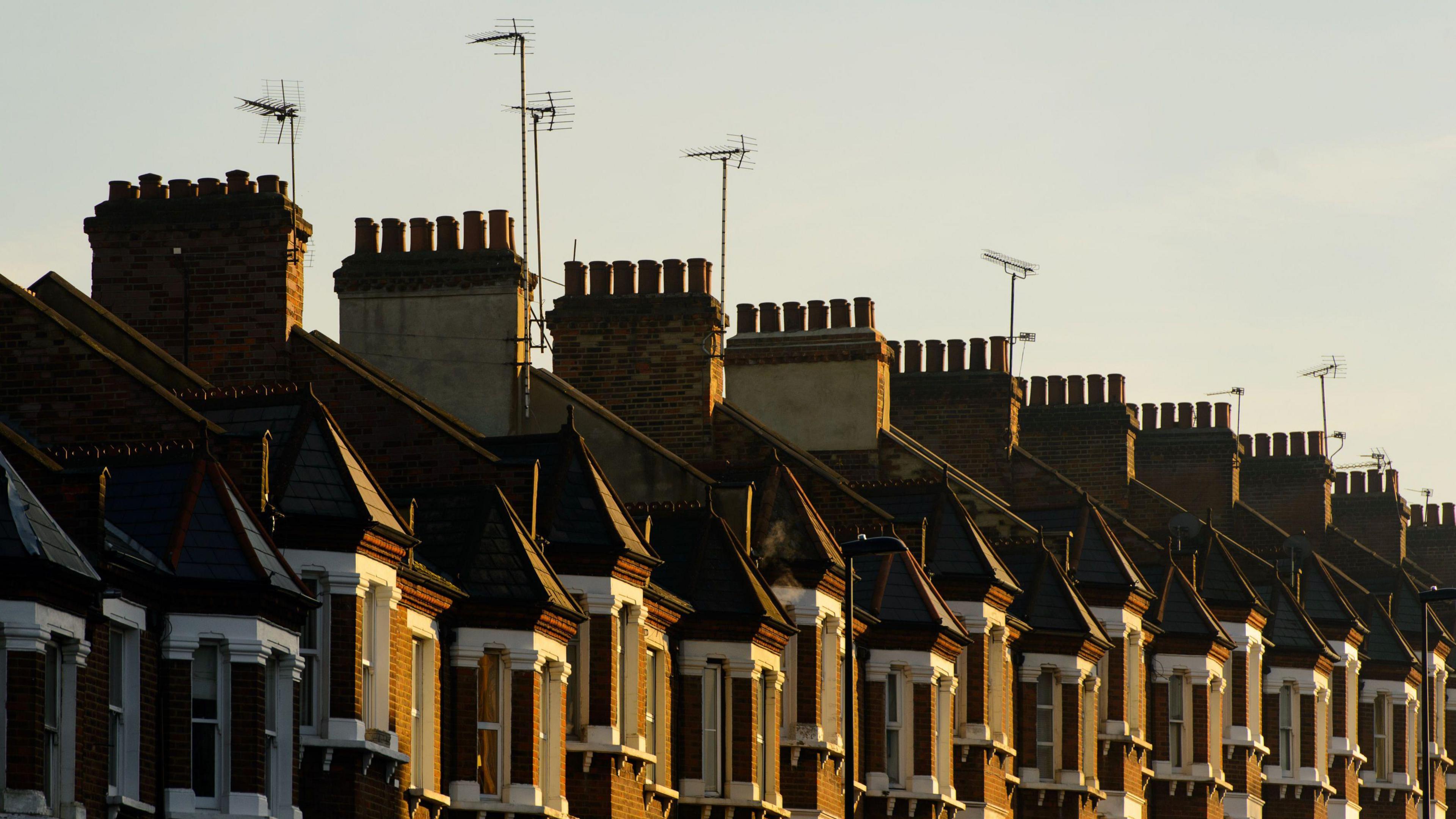 A row of terraced brick houses with chimneys and television aerials.
