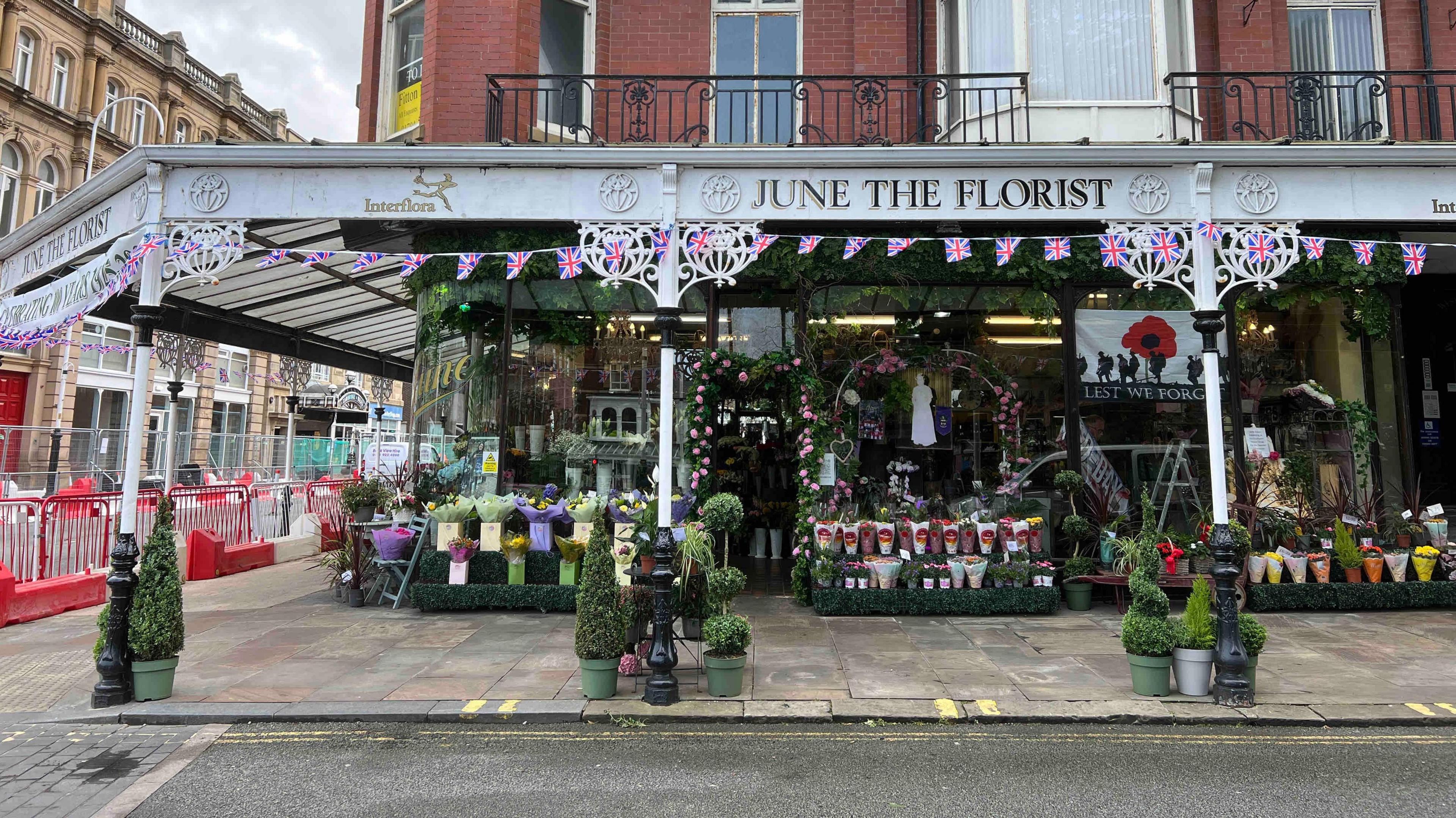 The outside of the shop, it has a white canopy with June the Florist written in gold lettering. The front is covered in flowers.