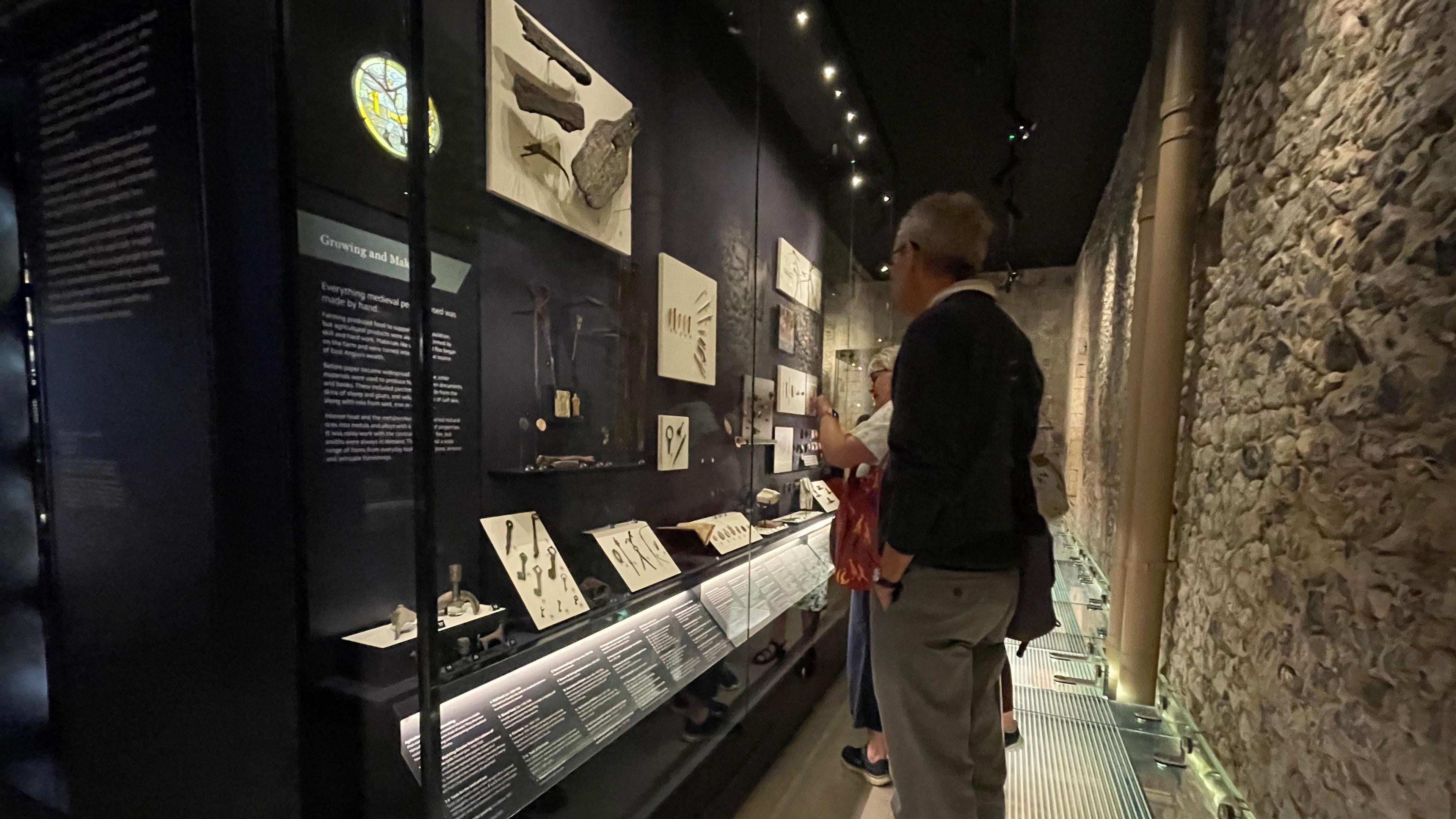 People looking at a display cabinet on the left which contains a range of items and text.