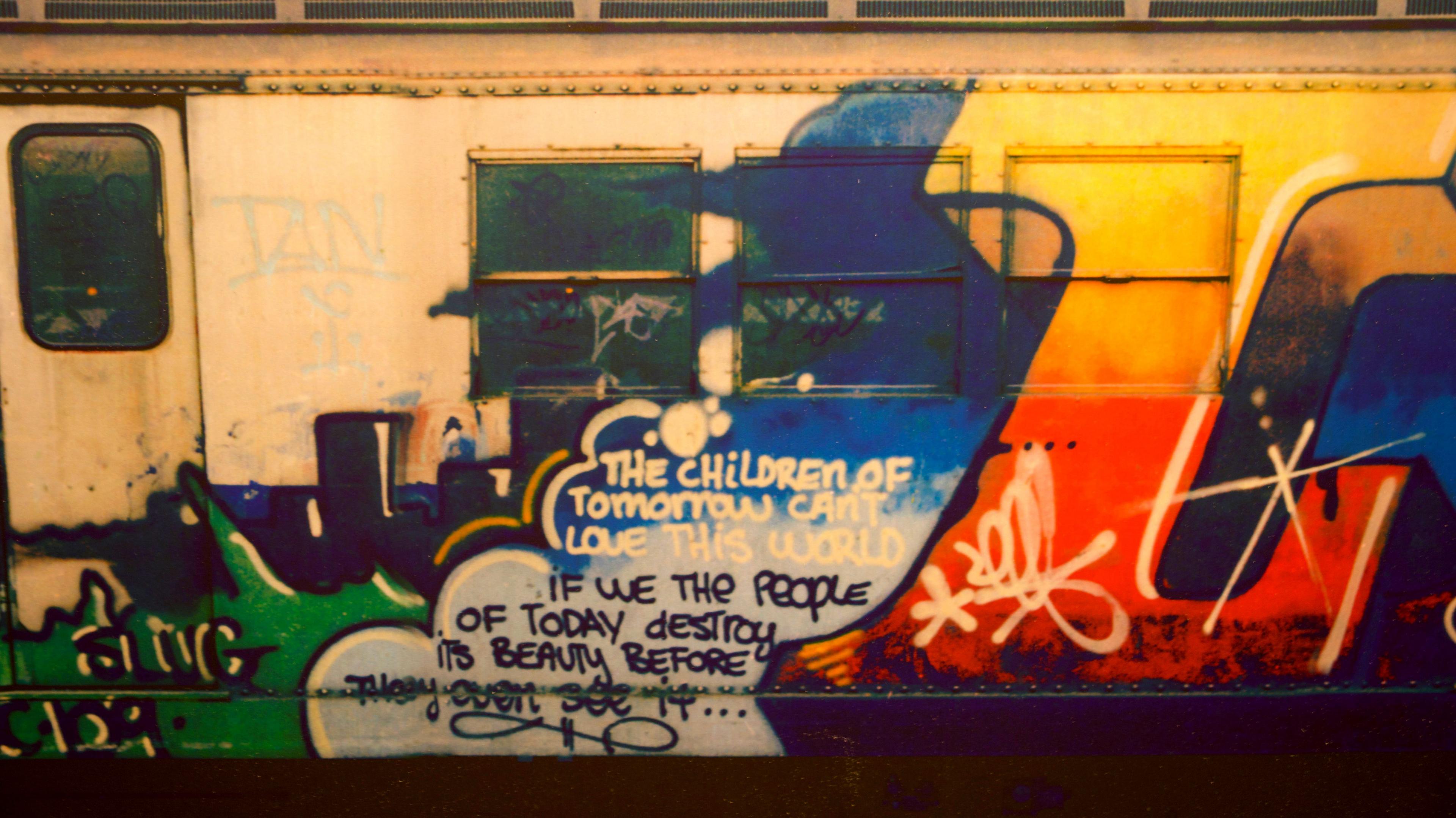 A subway train with green, blue and red graffiti and a message 'The children of tomorrow can't love this world if we the people of today destroy its beauty before they even see it'.