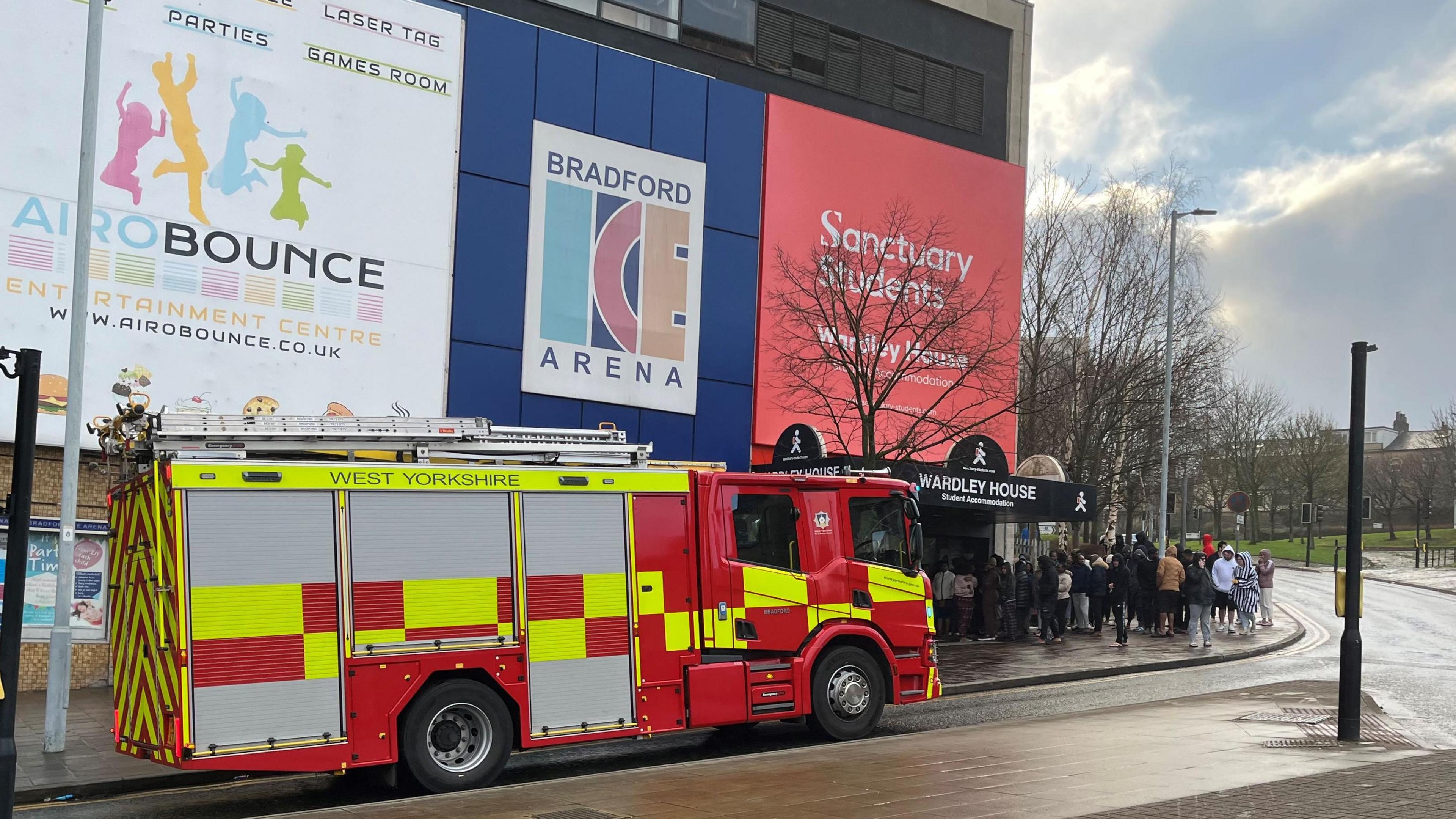 Fire engine at Wardley House in Bradford, with students waiting outside. The building carries signs advertising a trampoline park and an ice skating rink. 