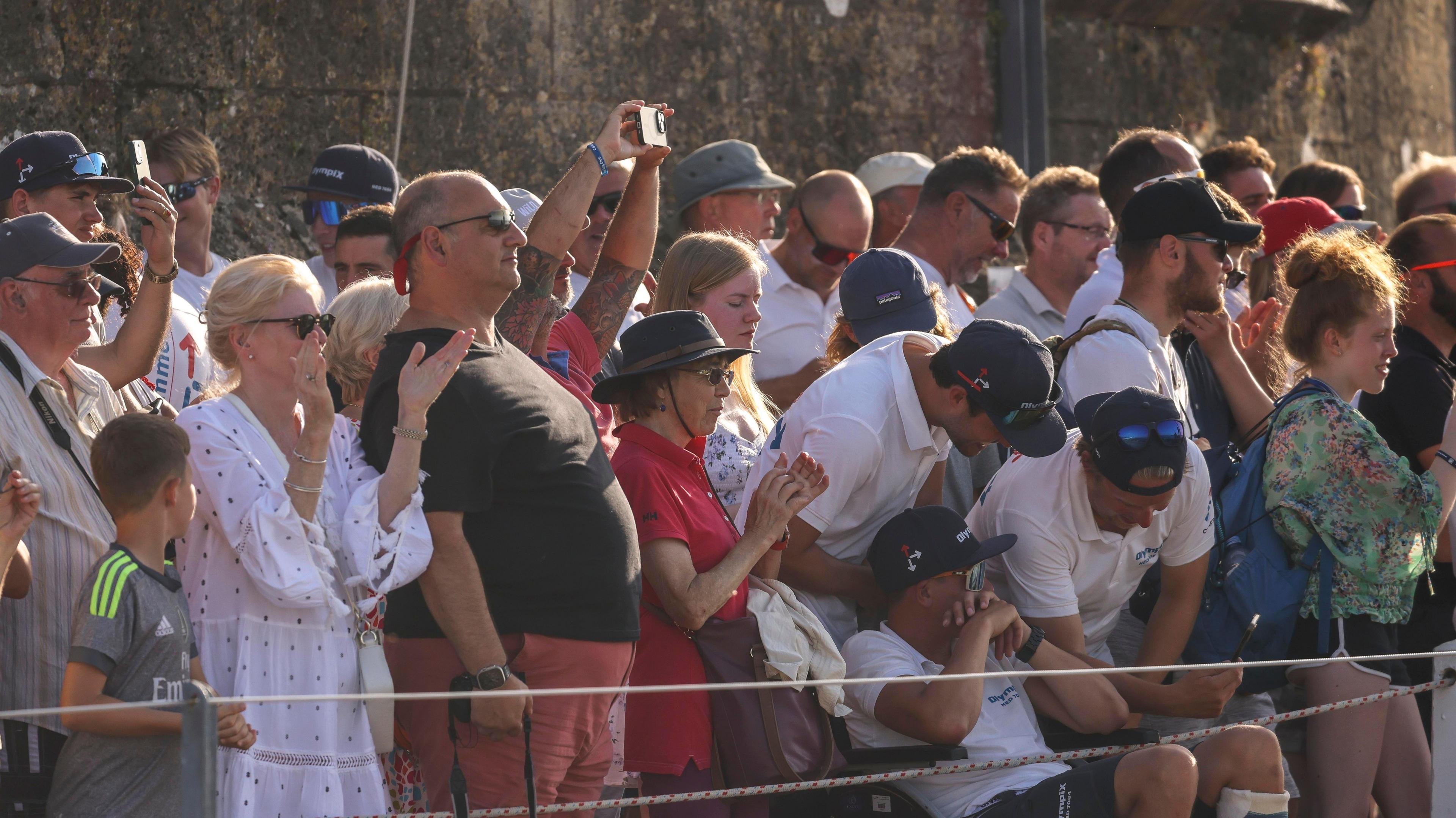 Crowds of people, some with phones out, in the evening sun