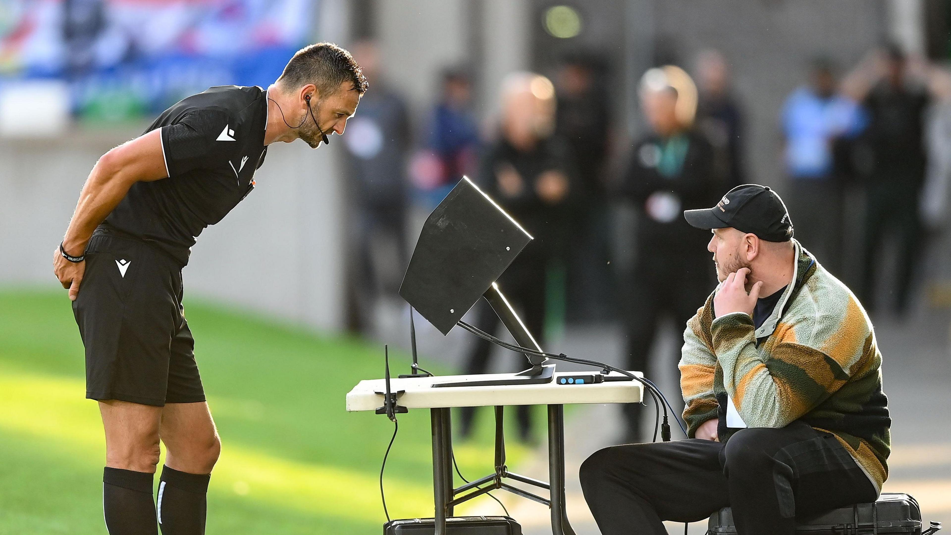 Referee Andrew Madley reviews a Shelbourne goal on the VAR monitor at Windsor Park