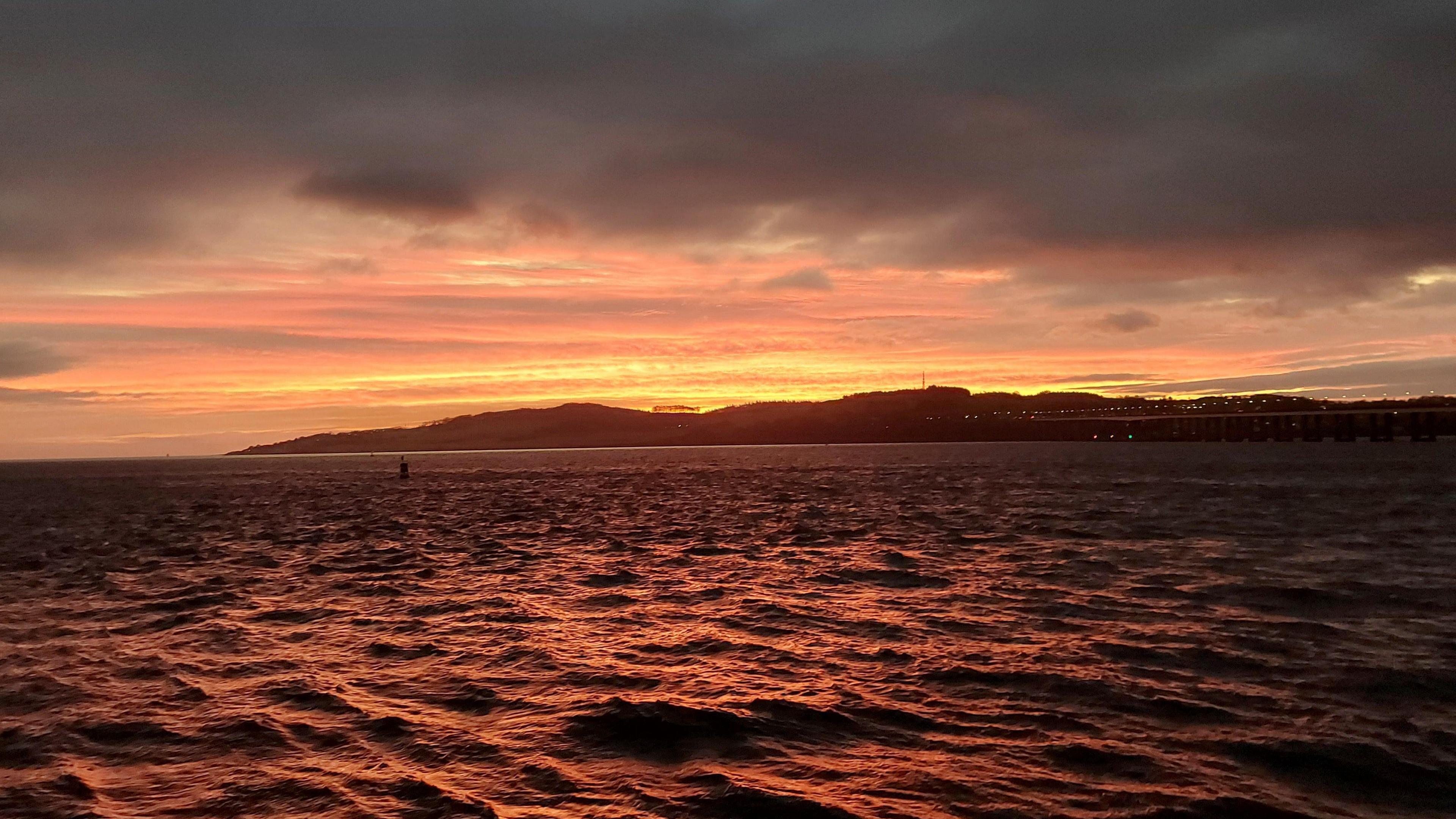 An orange and pink toned sunrise over the a choppy body of water.