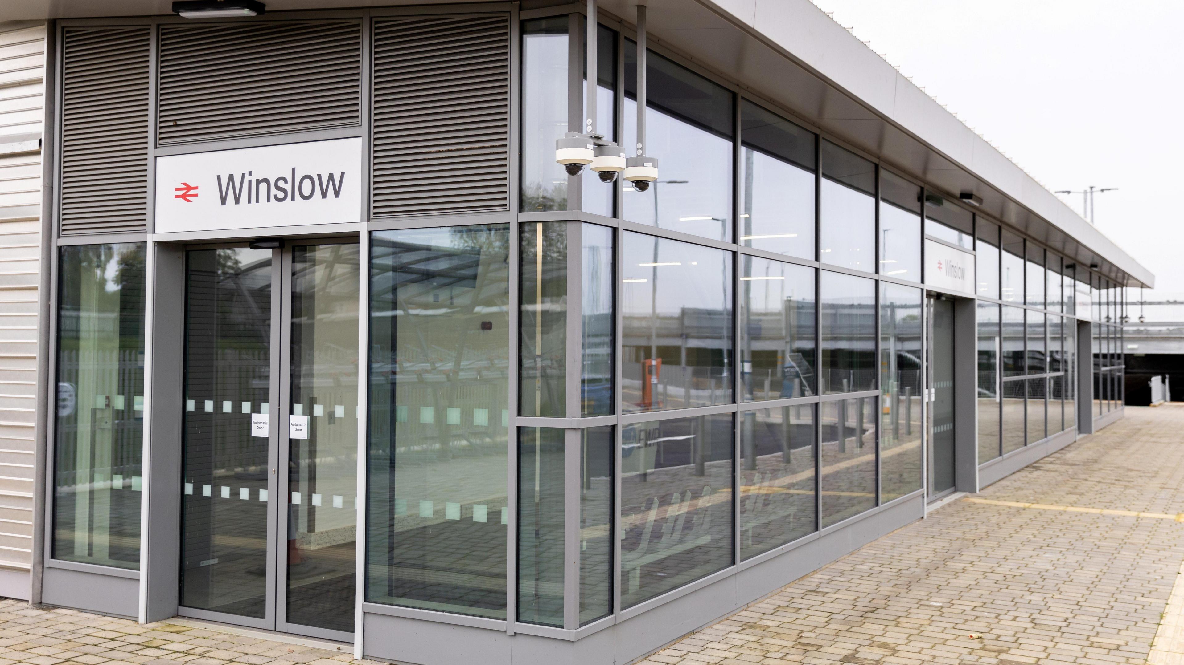 Winslow railway station, a grey building with lots of windows, in a box shape, with a paved front.