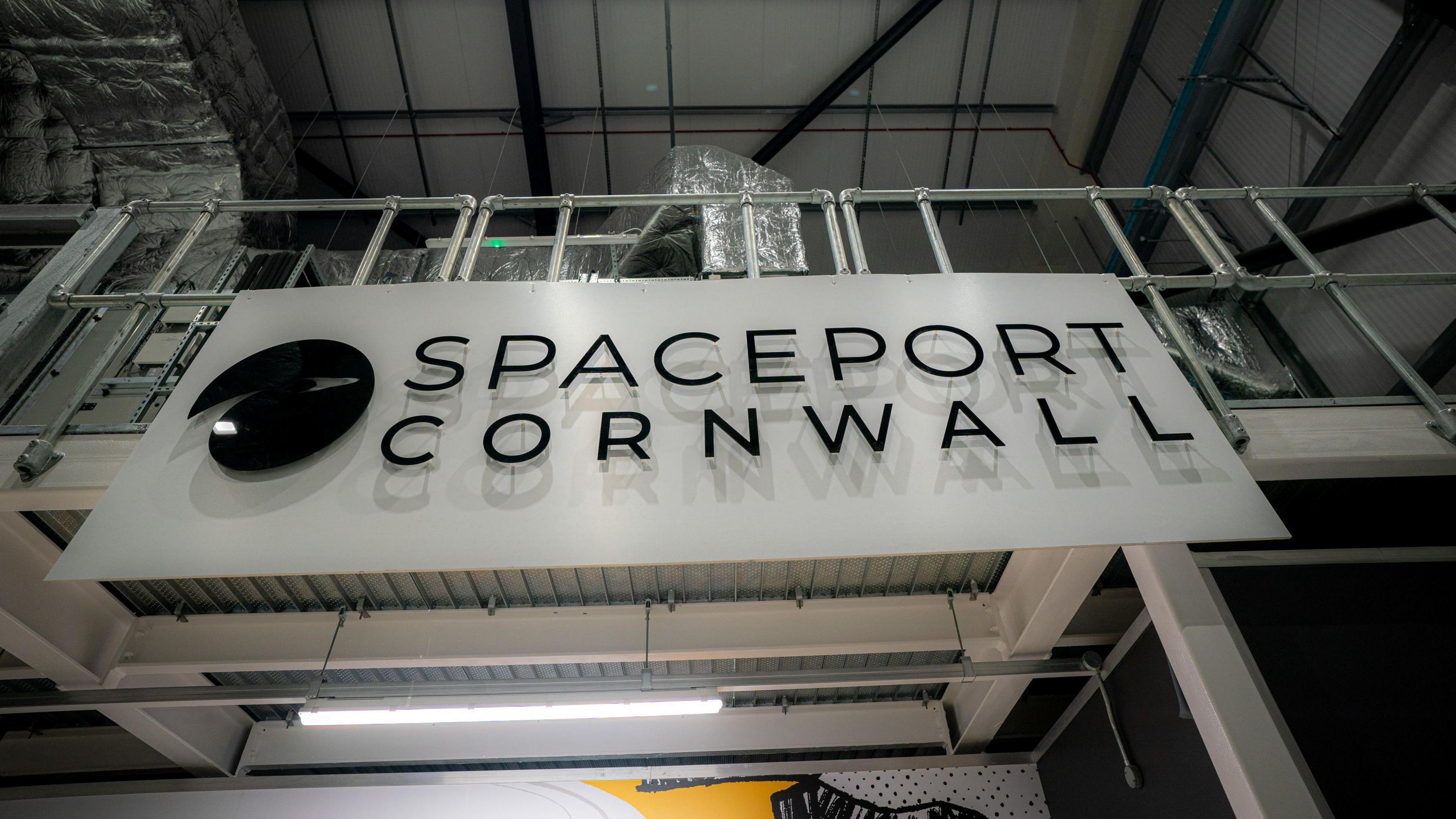 A black and white sign which says Spaceport Cornwall inside a building.