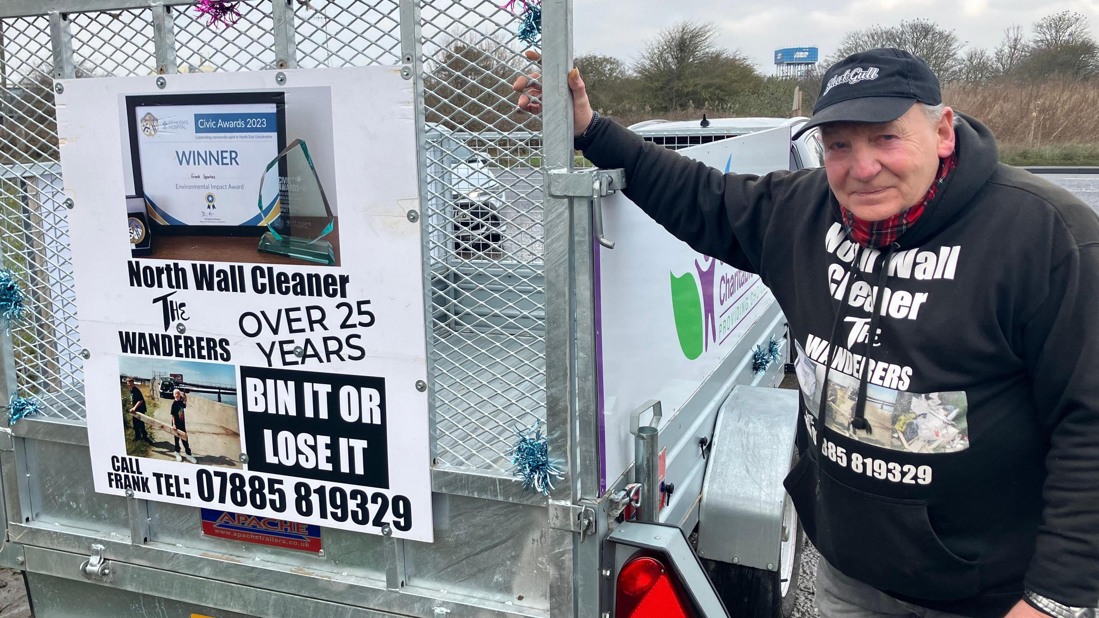 Frank Sparkes wearing a black top bearing his nickname - the North Wall Cleaner - standing at the side of a silver-coloured trailer.