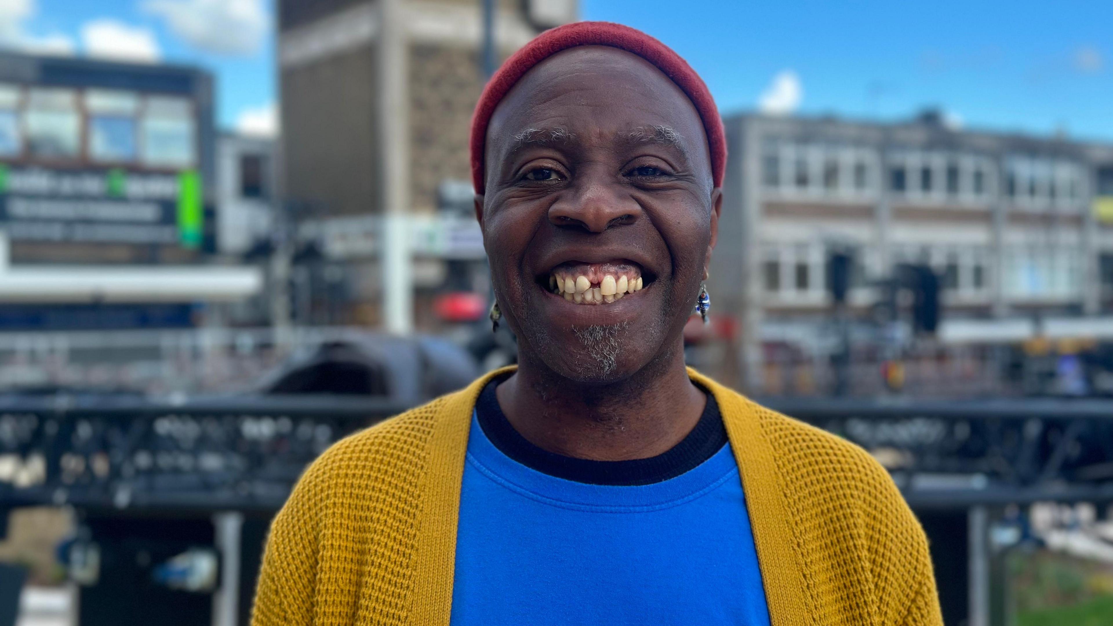 Picture of Musical director Tayo Akinbode, wearing a blue tshirt and mustard yellow cardigan and red hat 