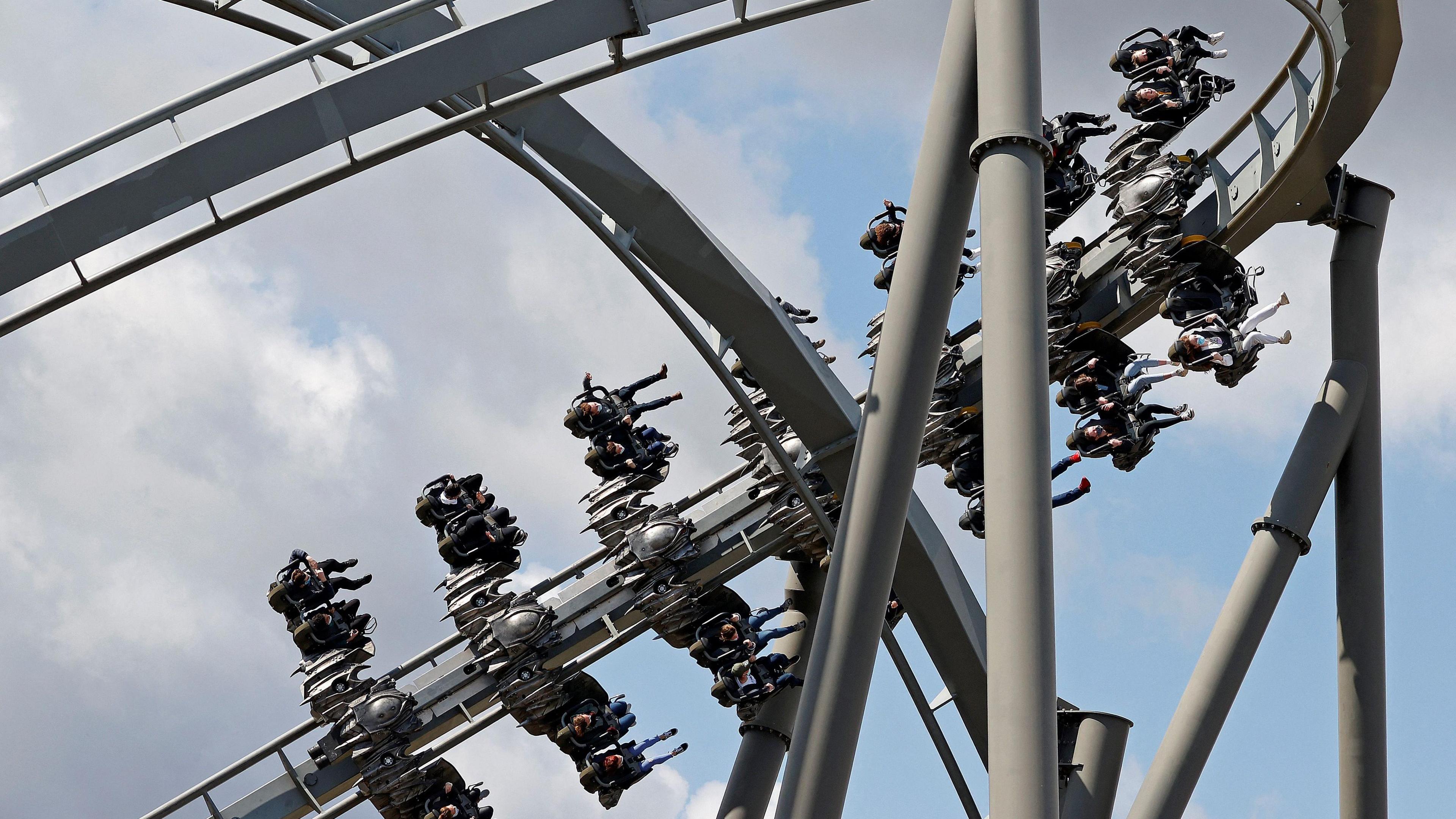 A huge silver-coloured rollercoaster  A group of people can be seen hurtling past on the ride, their legs dangling as the coaster takes them around its track.